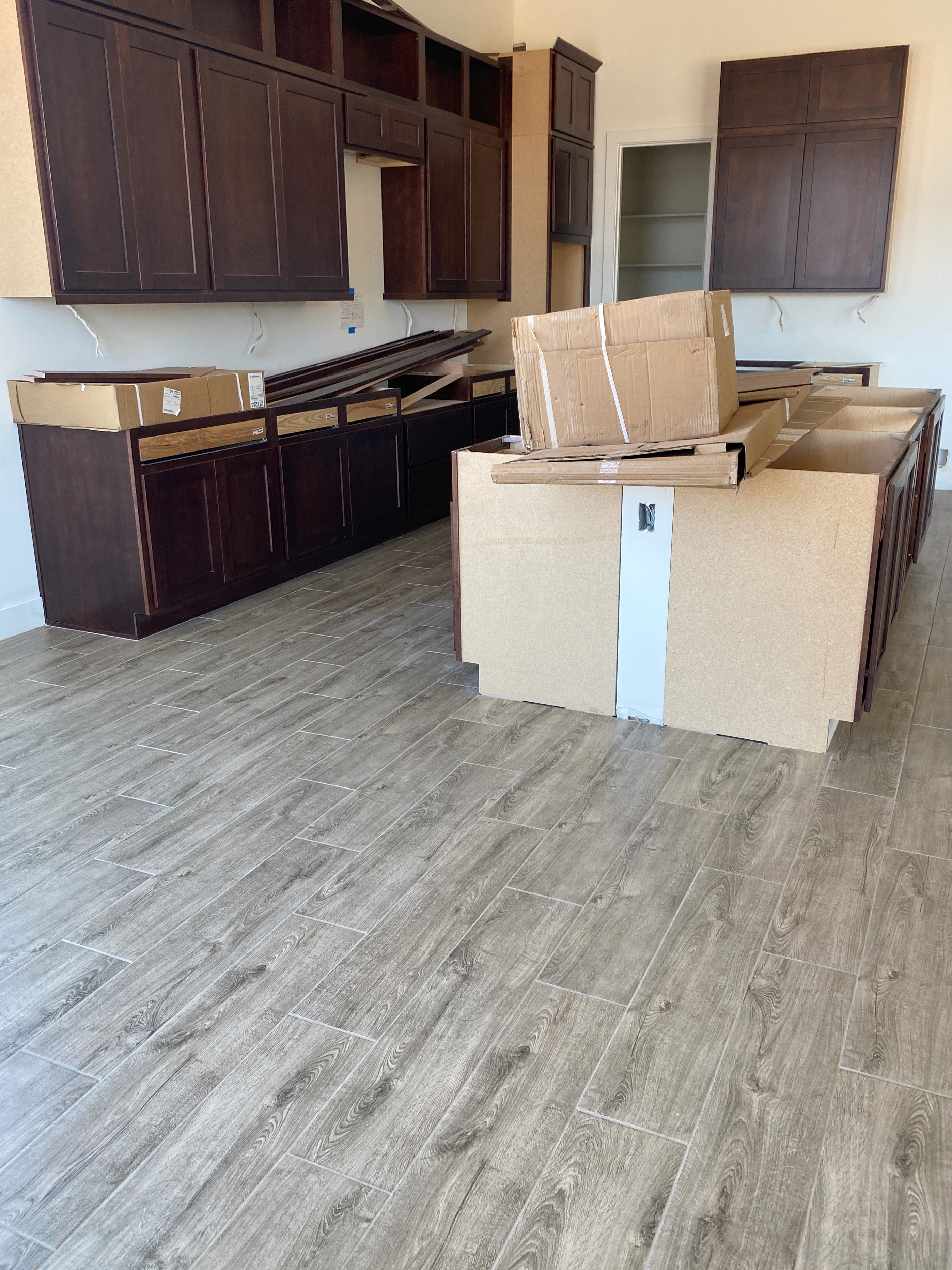 Modern kitchen with wood-look tile flooring, dark cabinets, and construction materials in a new home under construction.