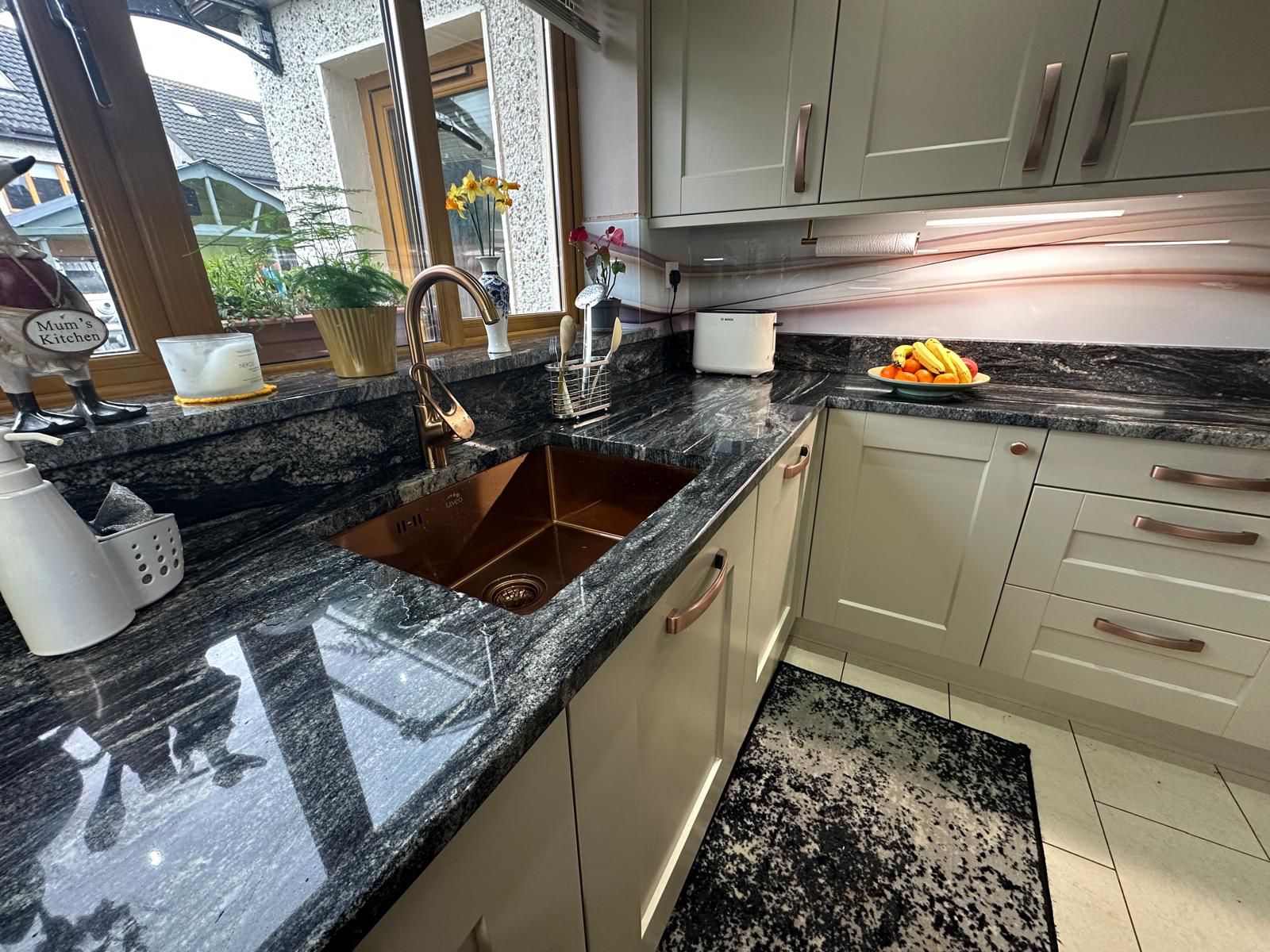 A serene outdoor seating area with two chairs, surrounded by lush greenery and a glassed-in structure.