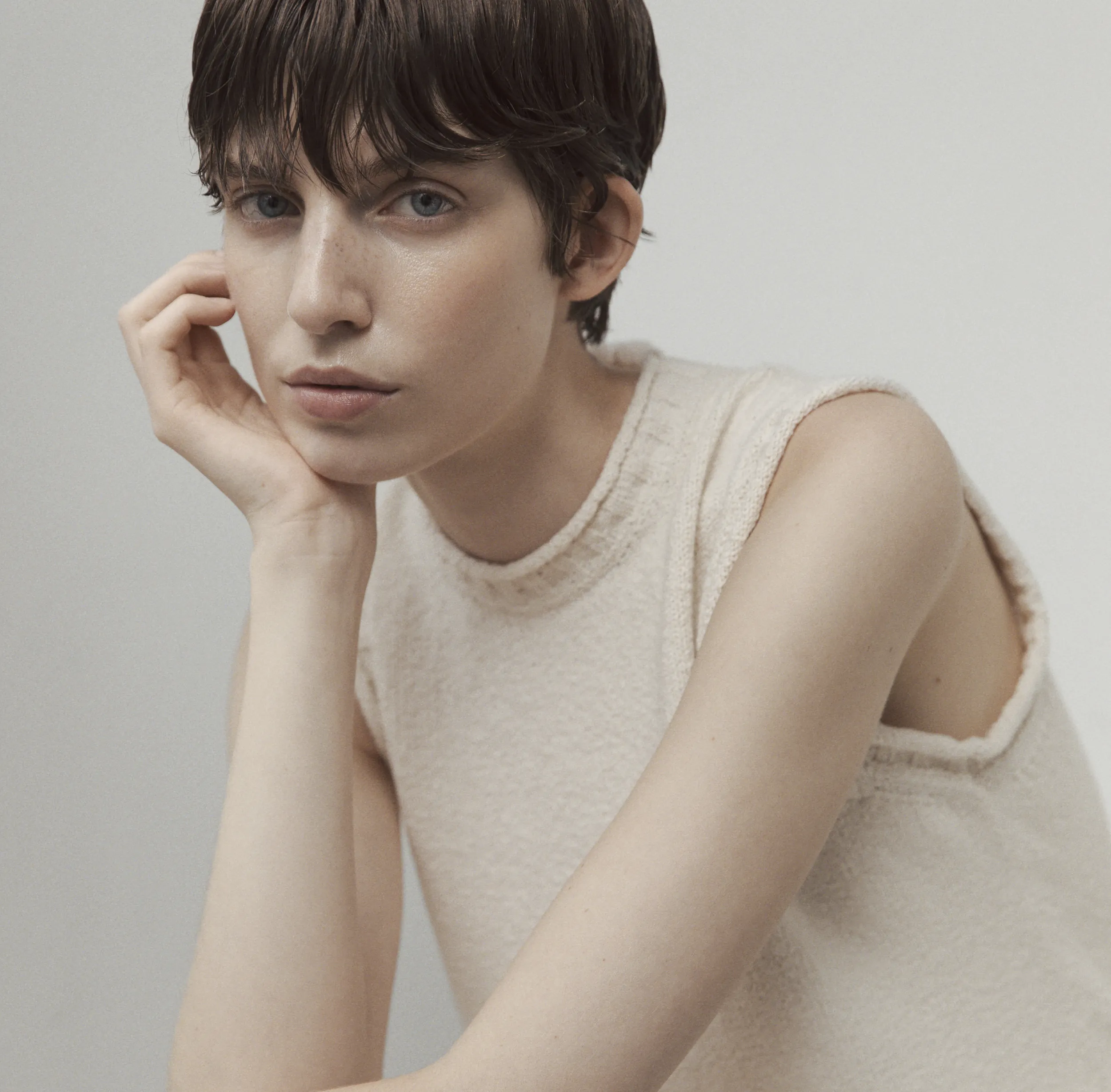 Close-up portrait of a model wearing the Aida Barni SS26 collection cream sleeveless knit dress, resting her face on her hand.