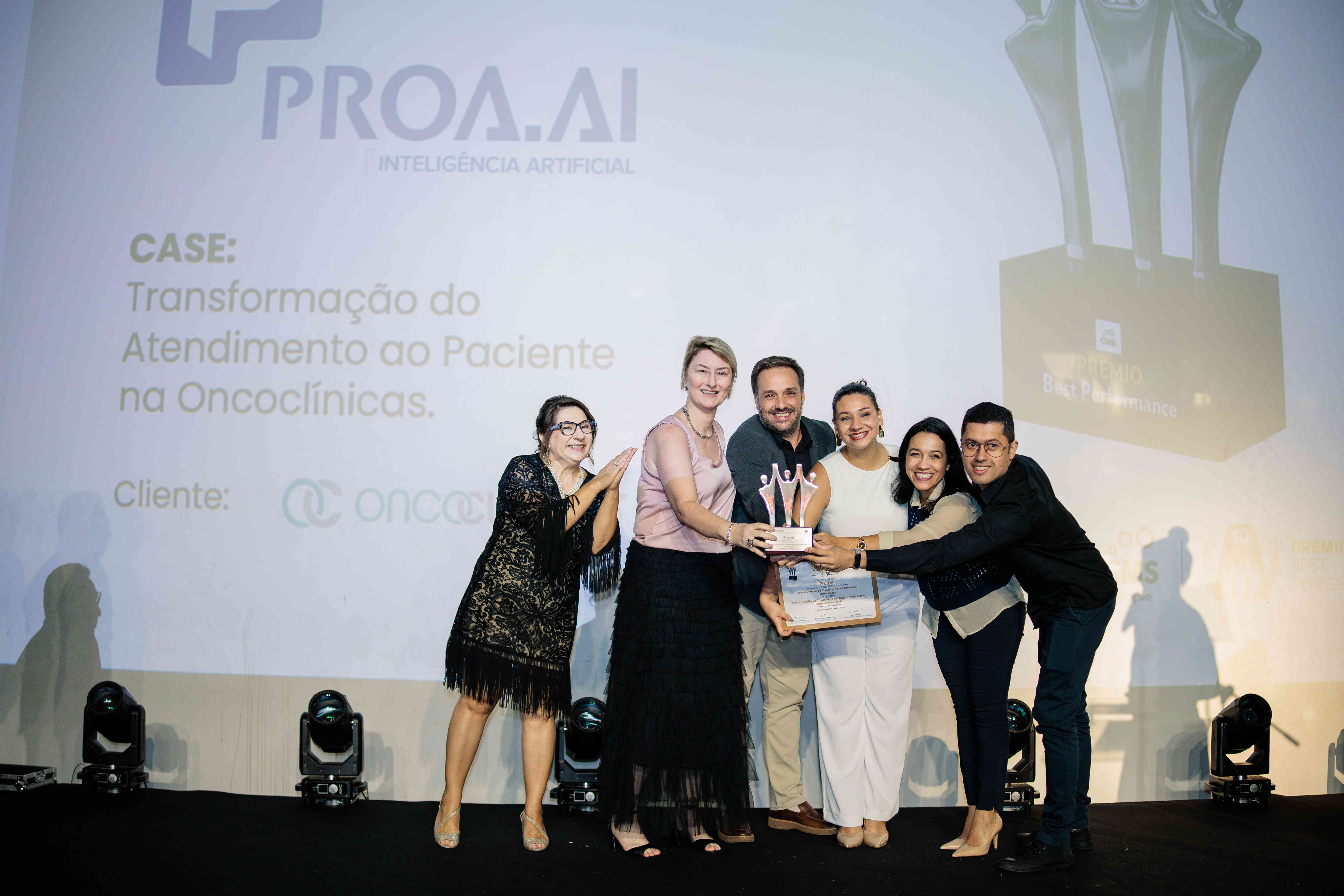 Executivos da Proa.ai posando com troféu prata e certificado no palco do Prêmio Best Performance 2025