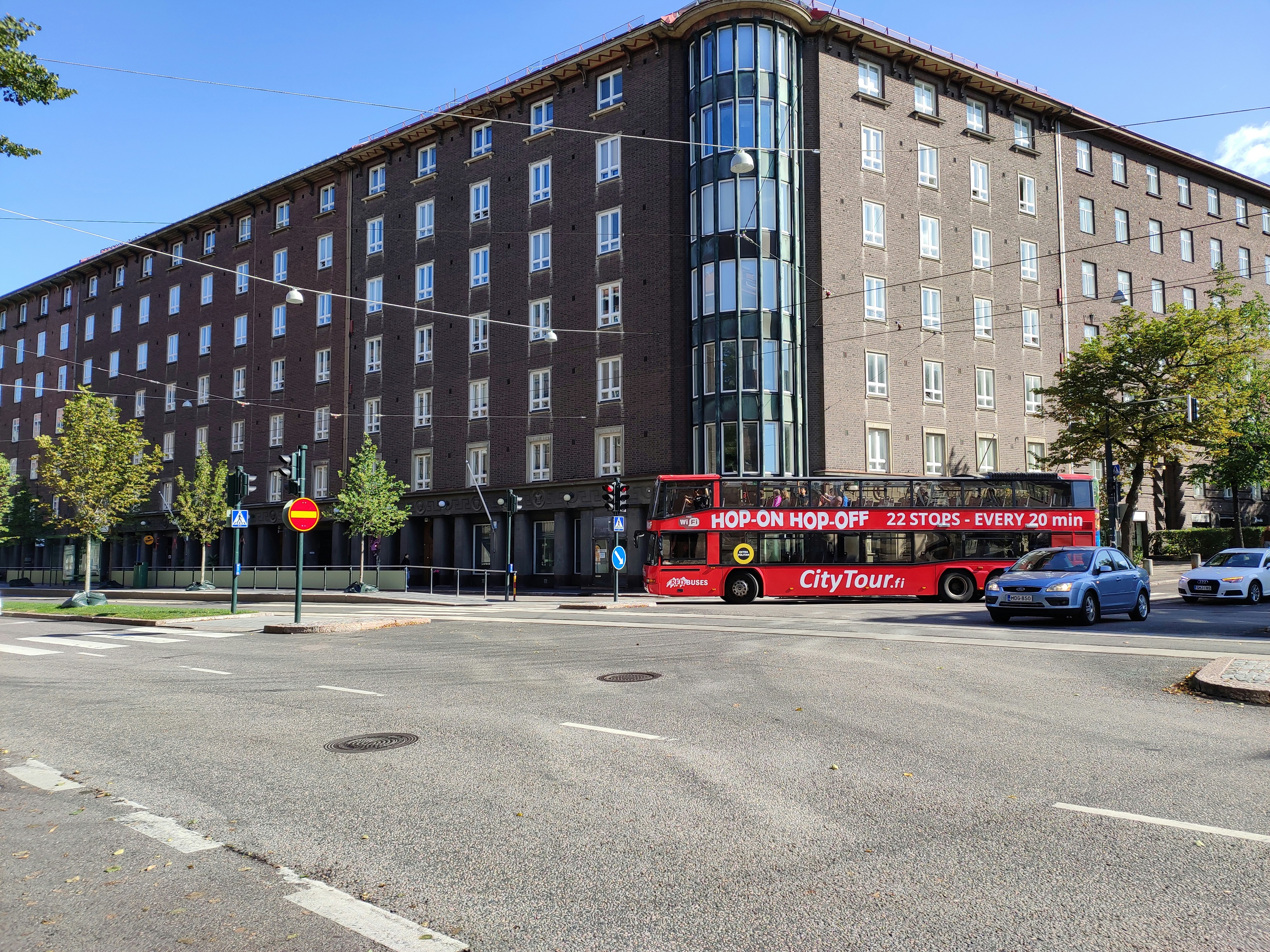 a red double decker bus driving past a tall building
