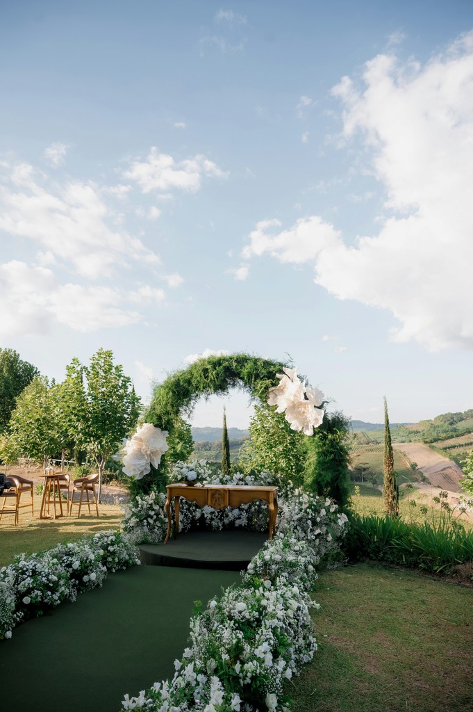 Wedding altar with a round greenery arch and white floral aisle leading to a vintage table on a hilltop with panoramic valley views