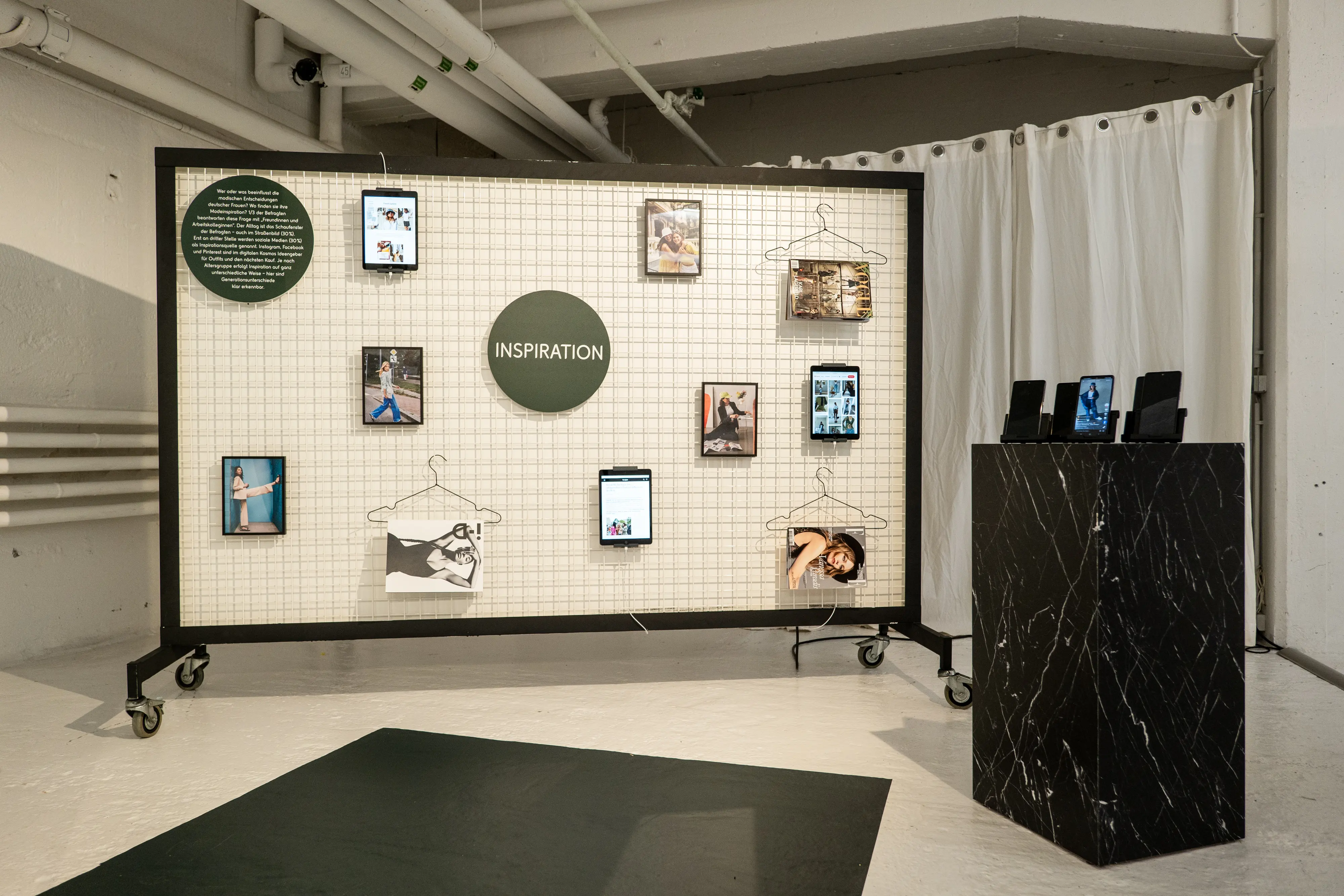 Inspiration board on wheels with tablets and photos on a grid, next to a black marble pedestal.