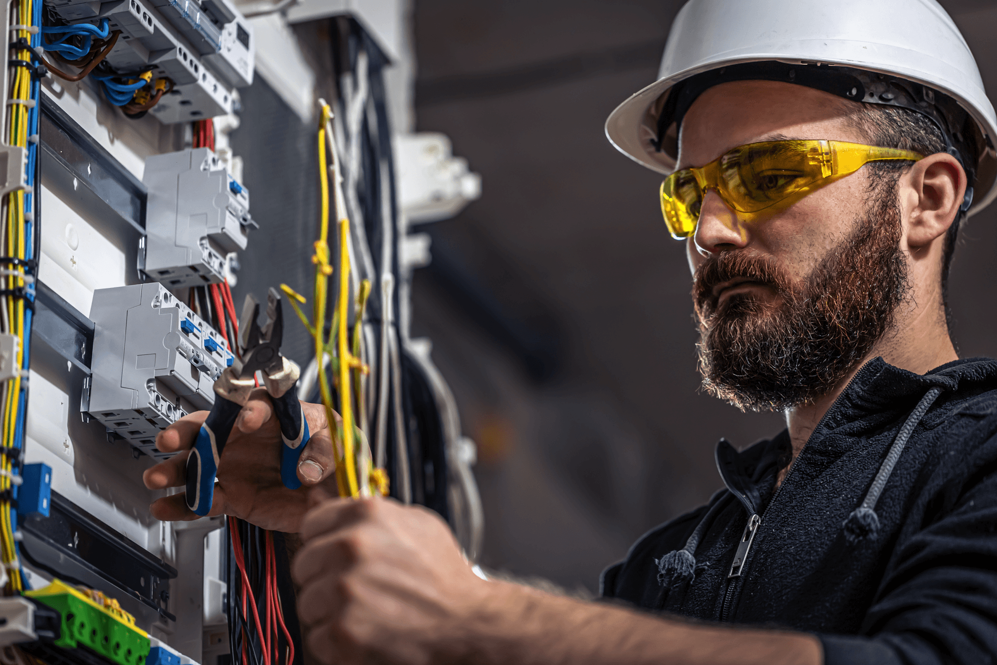 Técnico de eletricidade da TCC Especialização trabalhando em um painel elétrico, utilizando ferramentas de precisão. Profissional de engenharia elétrica usando equipamentos de segurança, como capacete e óculos de proteção, para garantir a instalação segura e eficaz de fiações.