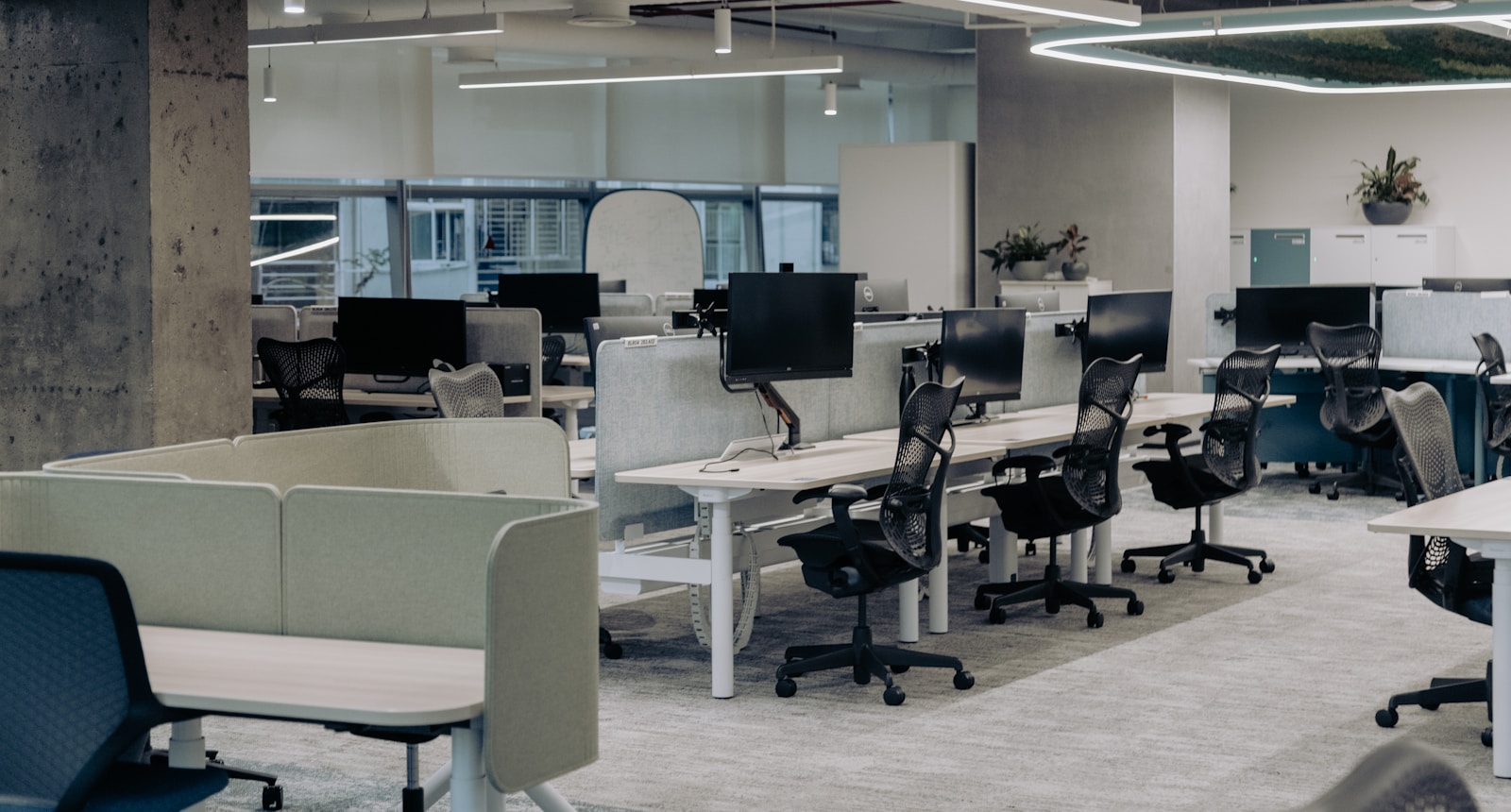 Bright modern office workspace with rows of clean desks, computers, glass walls and natural light