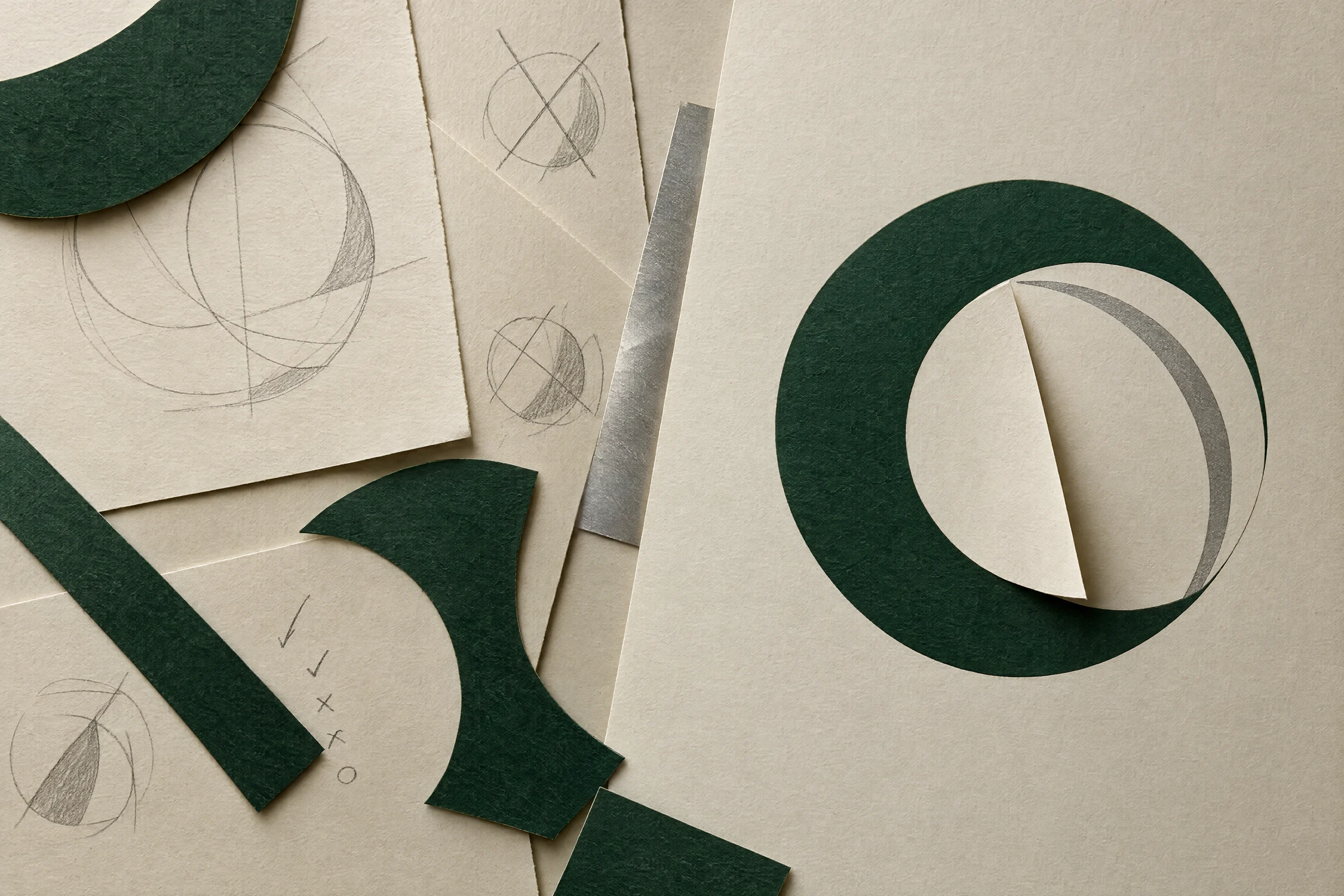 Graphite composition studies and cut green paper progressing to a finished circular frame.