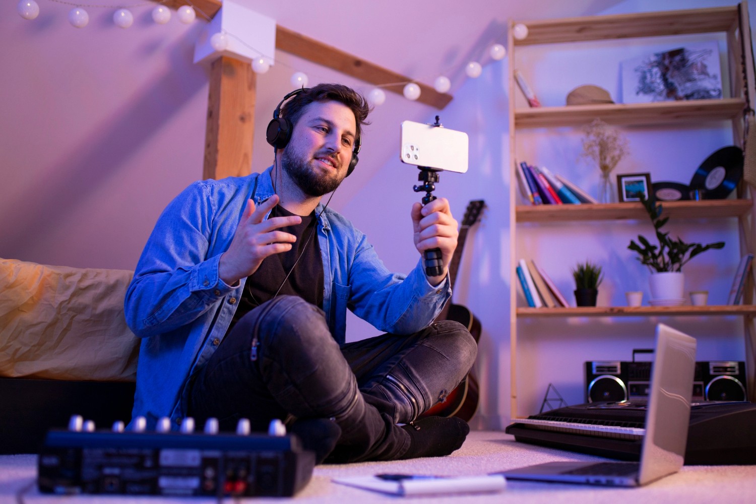 A man seated on the floor, focused on a camera beside a laptop, engaged in photography or editing work.