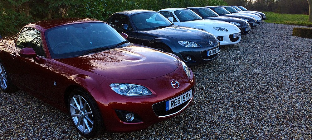 Front view of a powerful, aggressive-looking black sports car with red accents, partially shrouded in dramatic red and white smoke/mist against a red background.