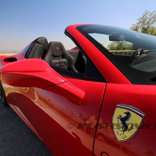 A red convertible sports car with a Ferrari logo on the door, parked on a road under a clear sky.