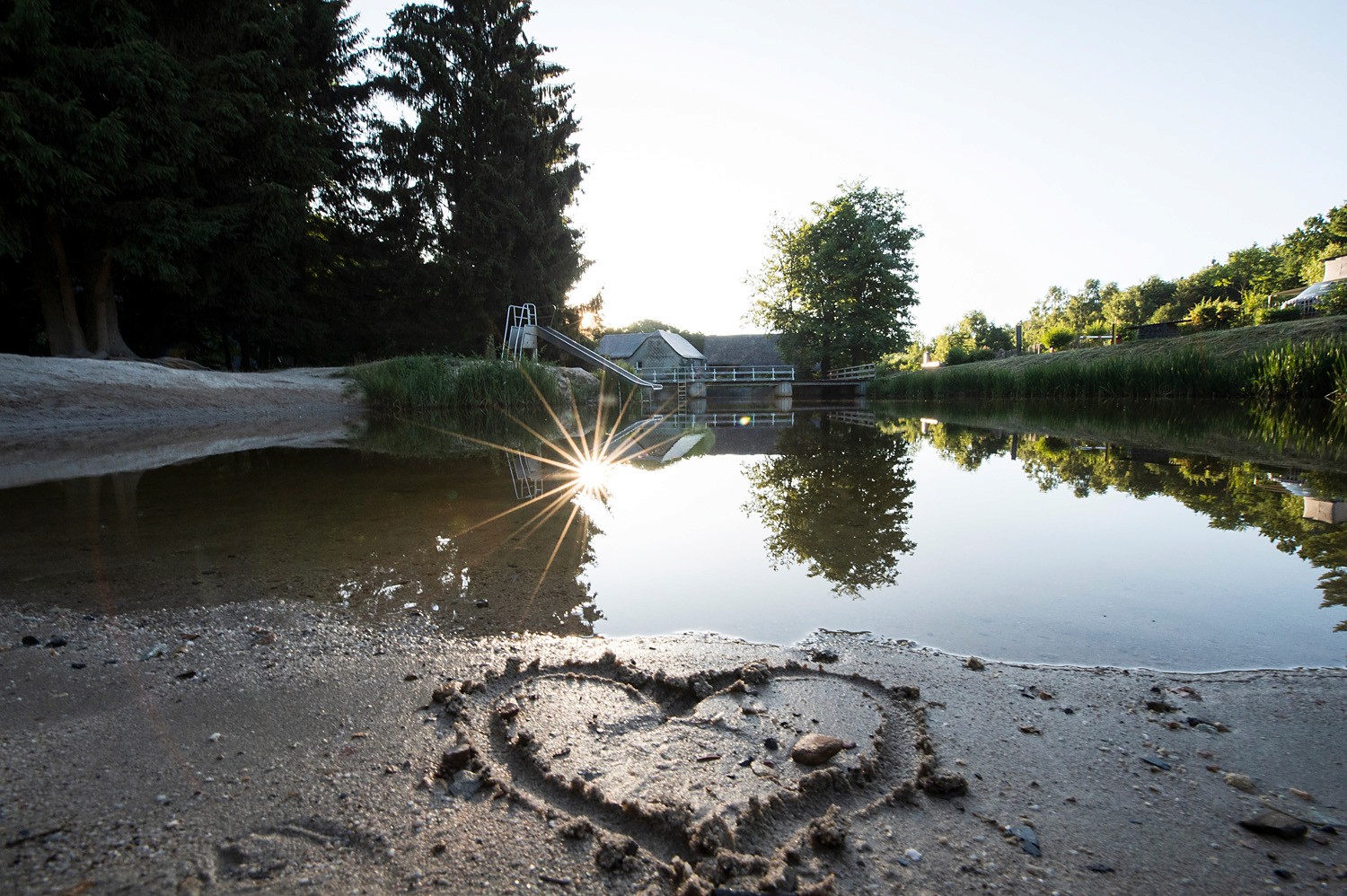 In the swimming lake, the sunrise reflects with the beach and a sand heart.