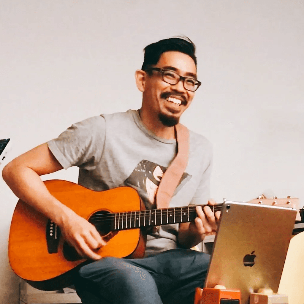A portrait shot of a smiling male person playing a guitar