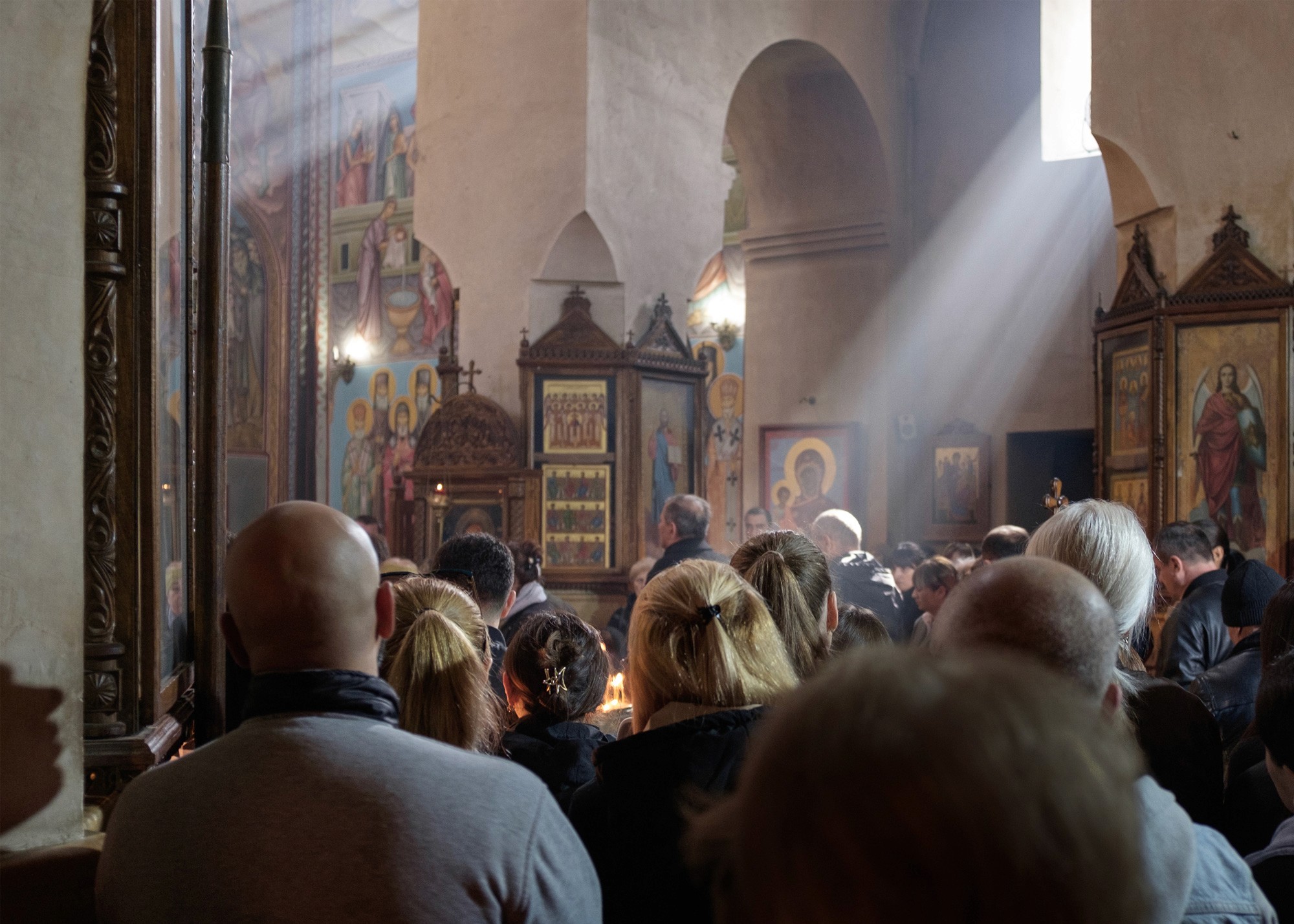 Mourners gather in a hillside cemetery during Tamaz Ginturi’s funeral. Dozens of people stand among parked cars and graves, overlooking a vast landscape of fields and mountains.