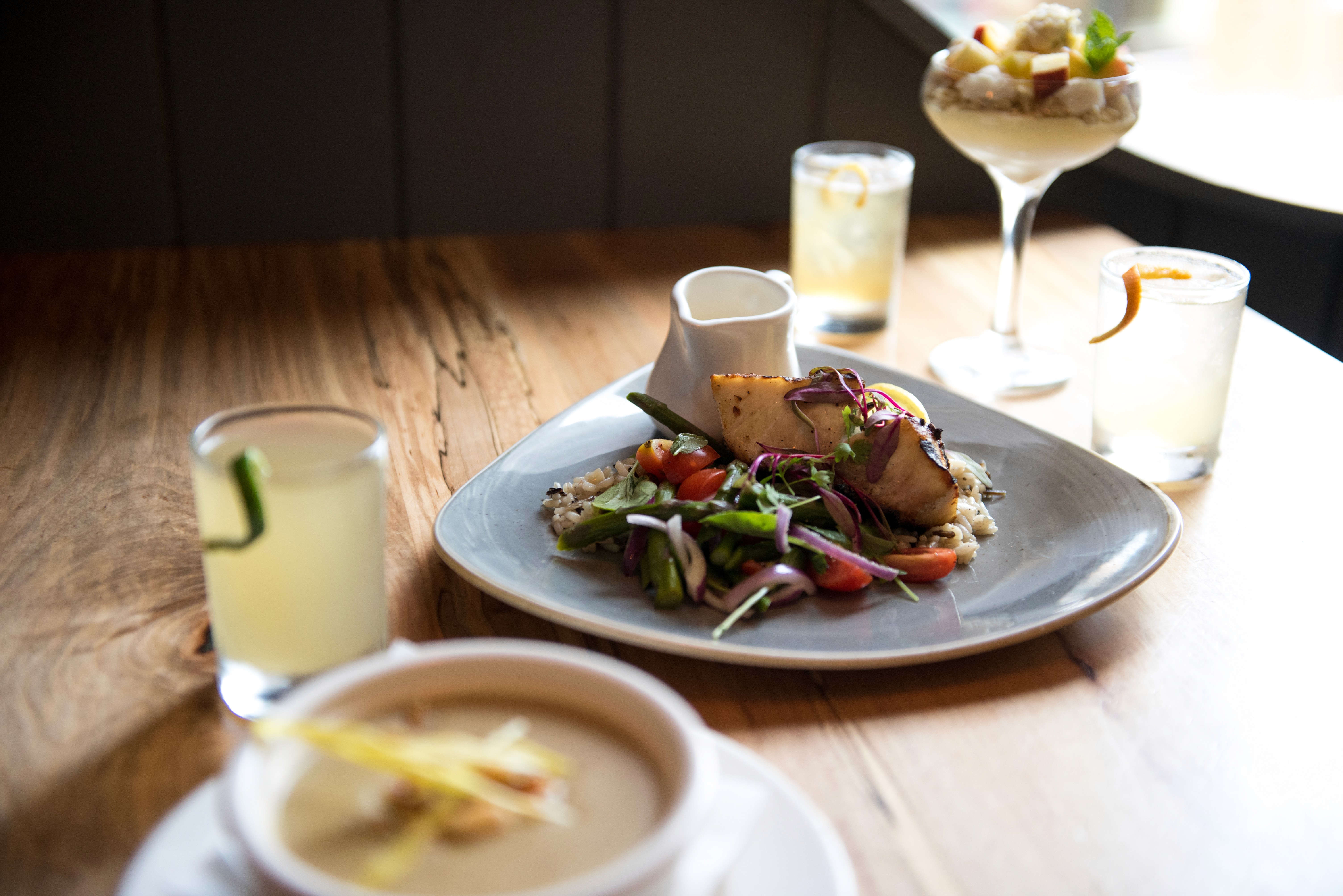 Product photography of a craft beer sitting in front of stainless steel tanks. The final beer has been poured into a shaped glass showcasing a hazy, golden liquid. 