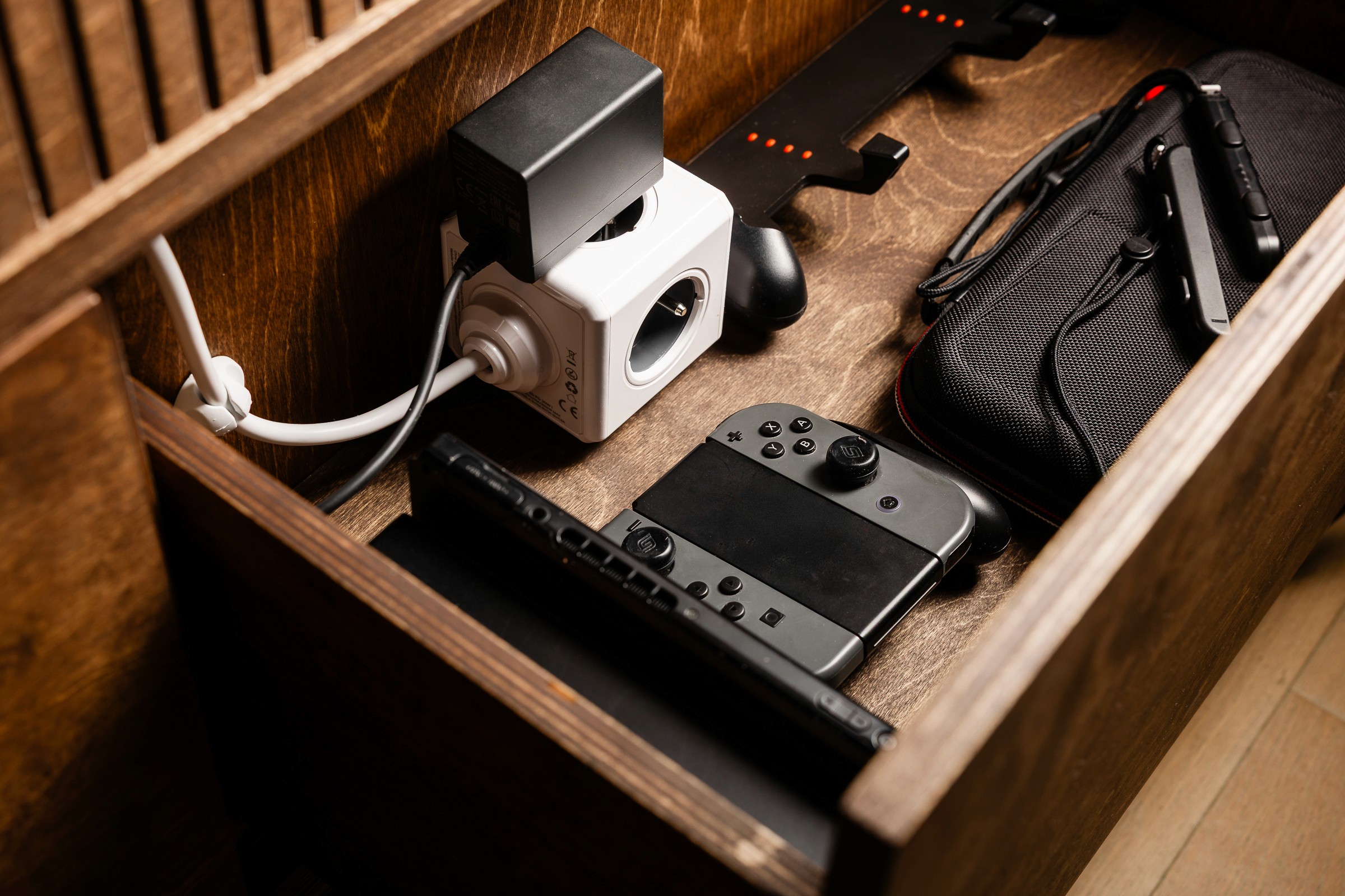 een lade van een tv-meubel waarin een gameconsole is verwerkt inclusief aansluiting op een stekkerblok