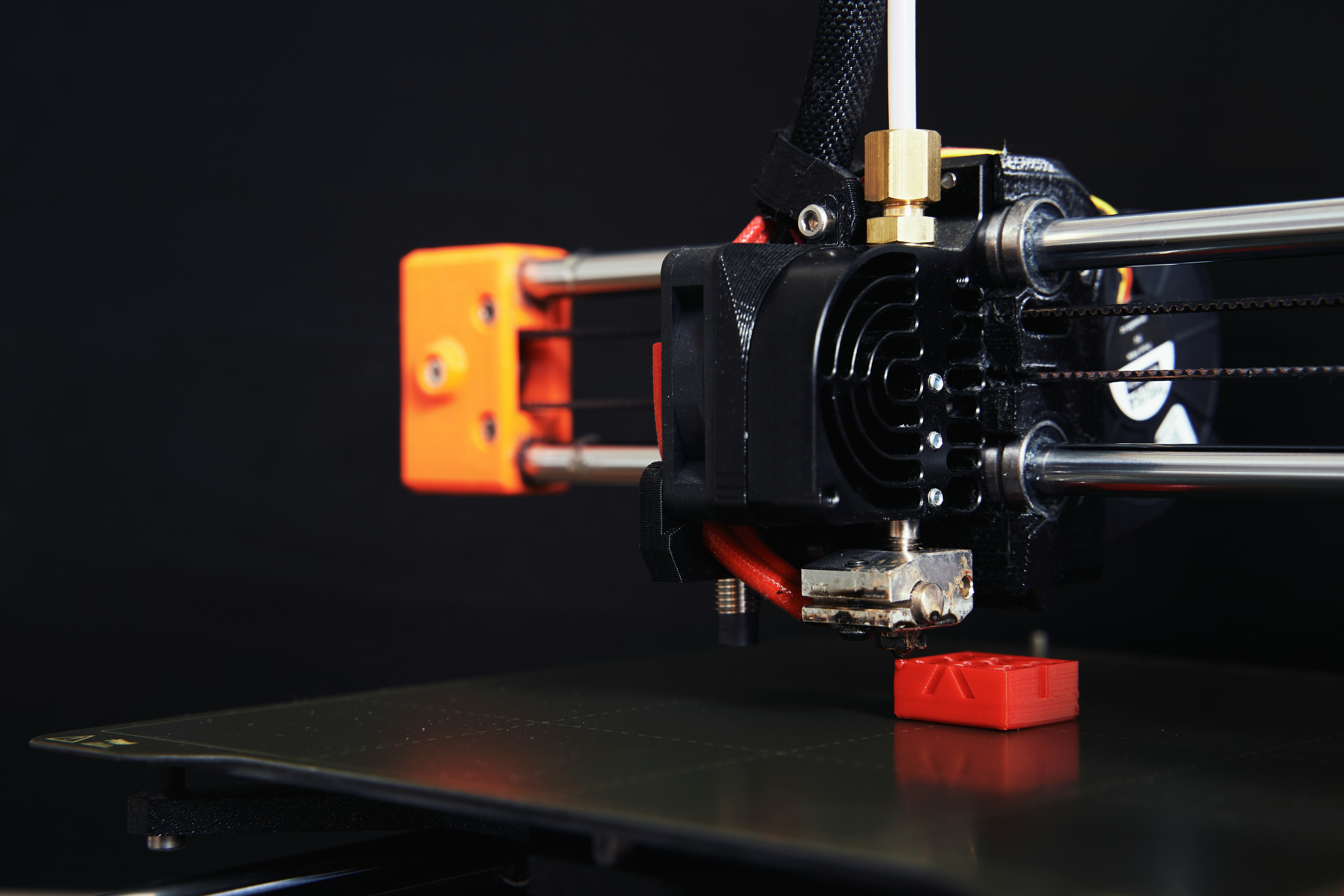 Close-up of a desktop FDM 3D printer extruder printing a small red model
