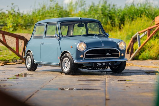 Een vintage blauwe auto geparkeerd op een zonnige dag, omringd door groen en een industriële achtergrond.