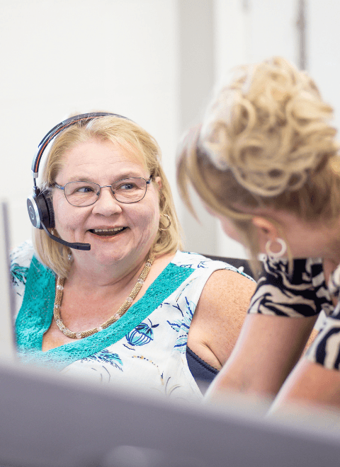 Two women, one with a headset on talking and smiling.