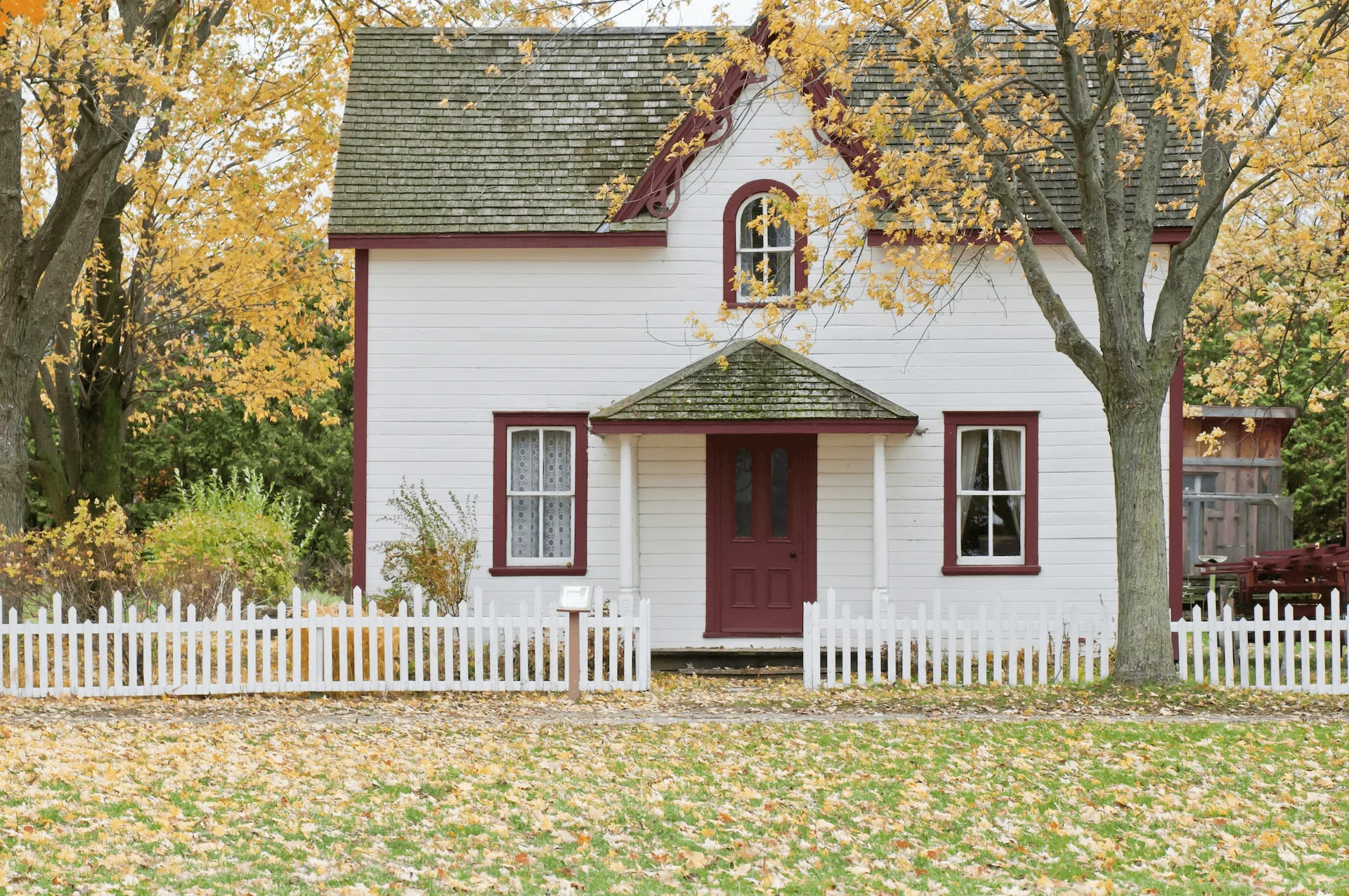 Small house with white fence and trees at the backyard, front lawn is wide