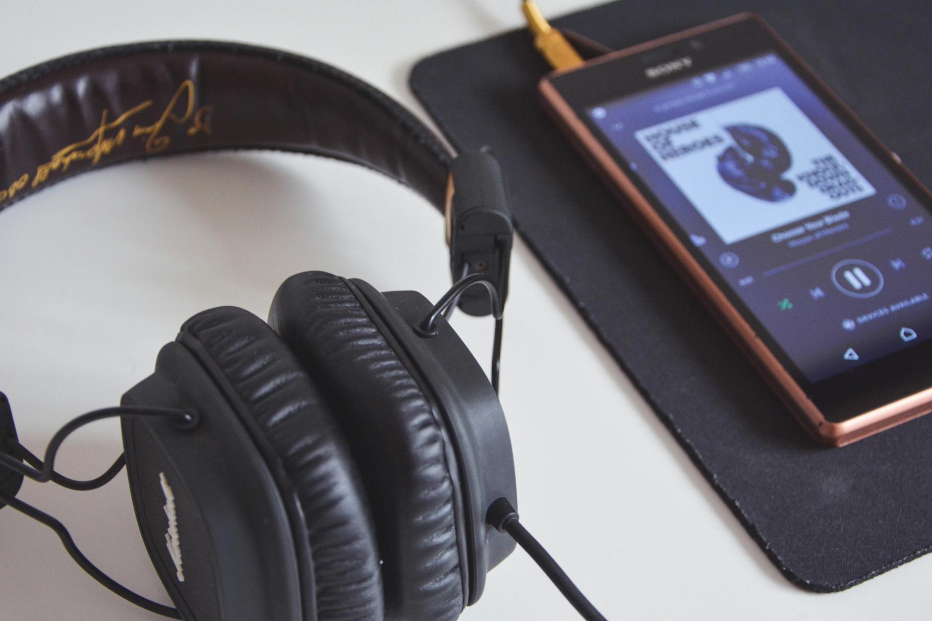 A close-up of a wooden desk featuring a smartphone with earbuds, a leather planner, and a focused checklist.