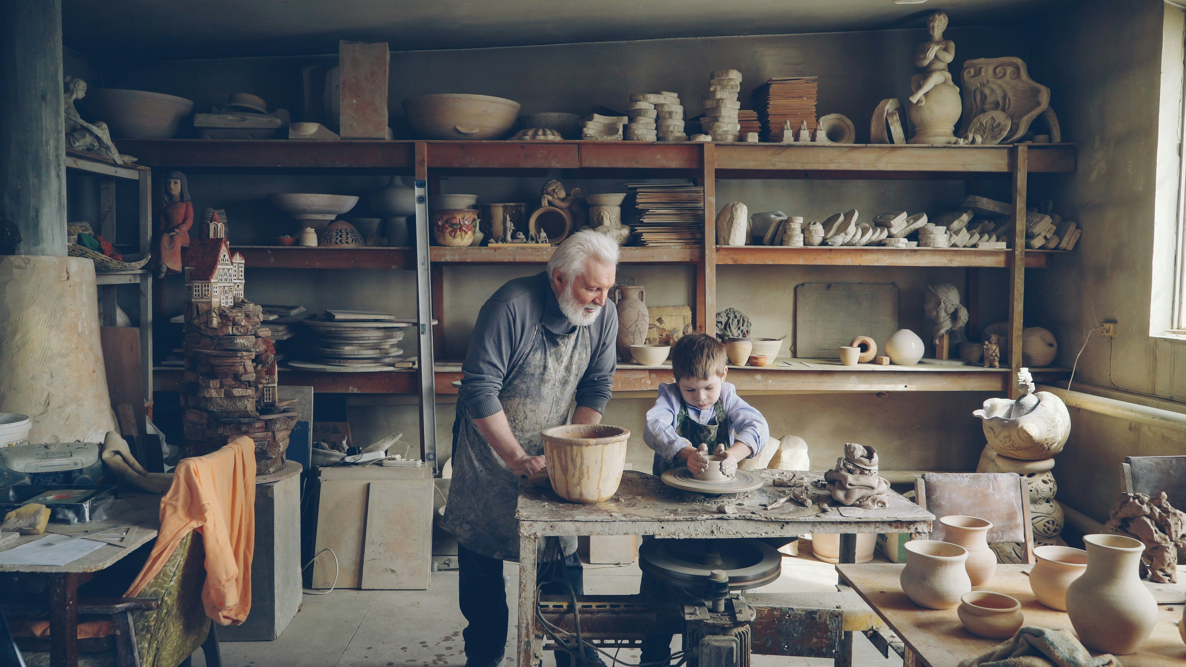 Grandfather and child craft pottery together in a studio.