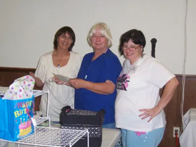 Three women sorting supplies and a birthday gift bag at a crop