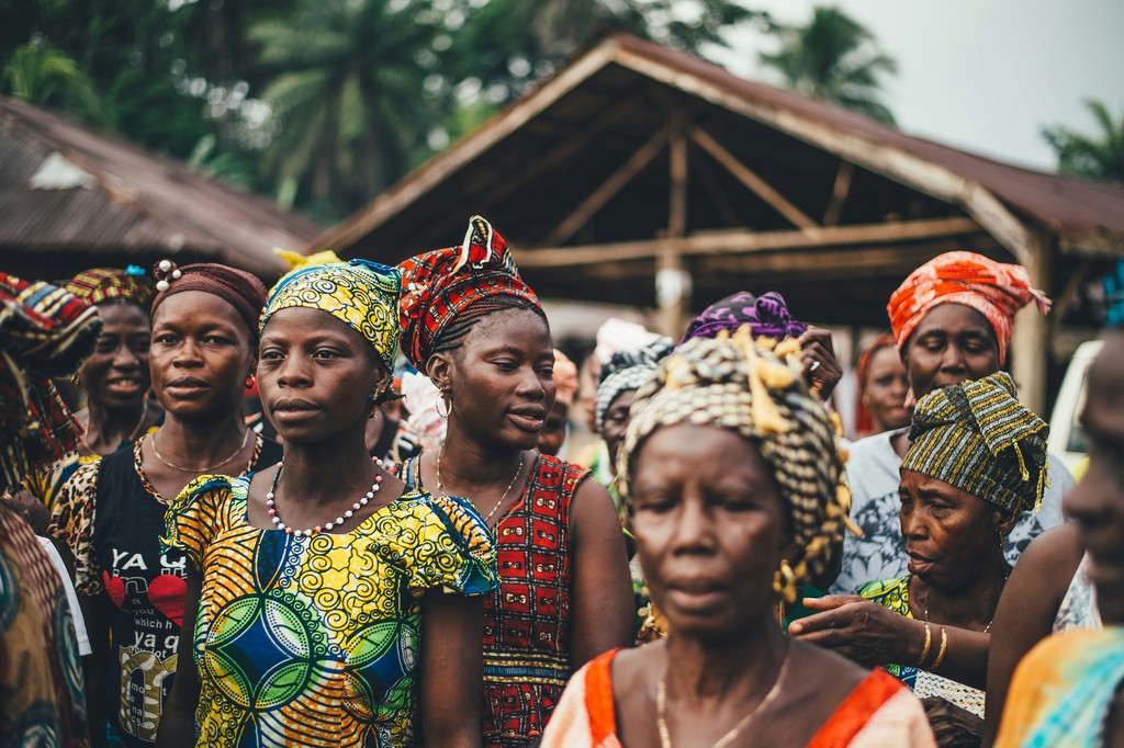 A group of women in colorful traditional attire gathers outdoors, engaging in conversation and celebration, reflecting the vibrant cultural heritage and community spirit.