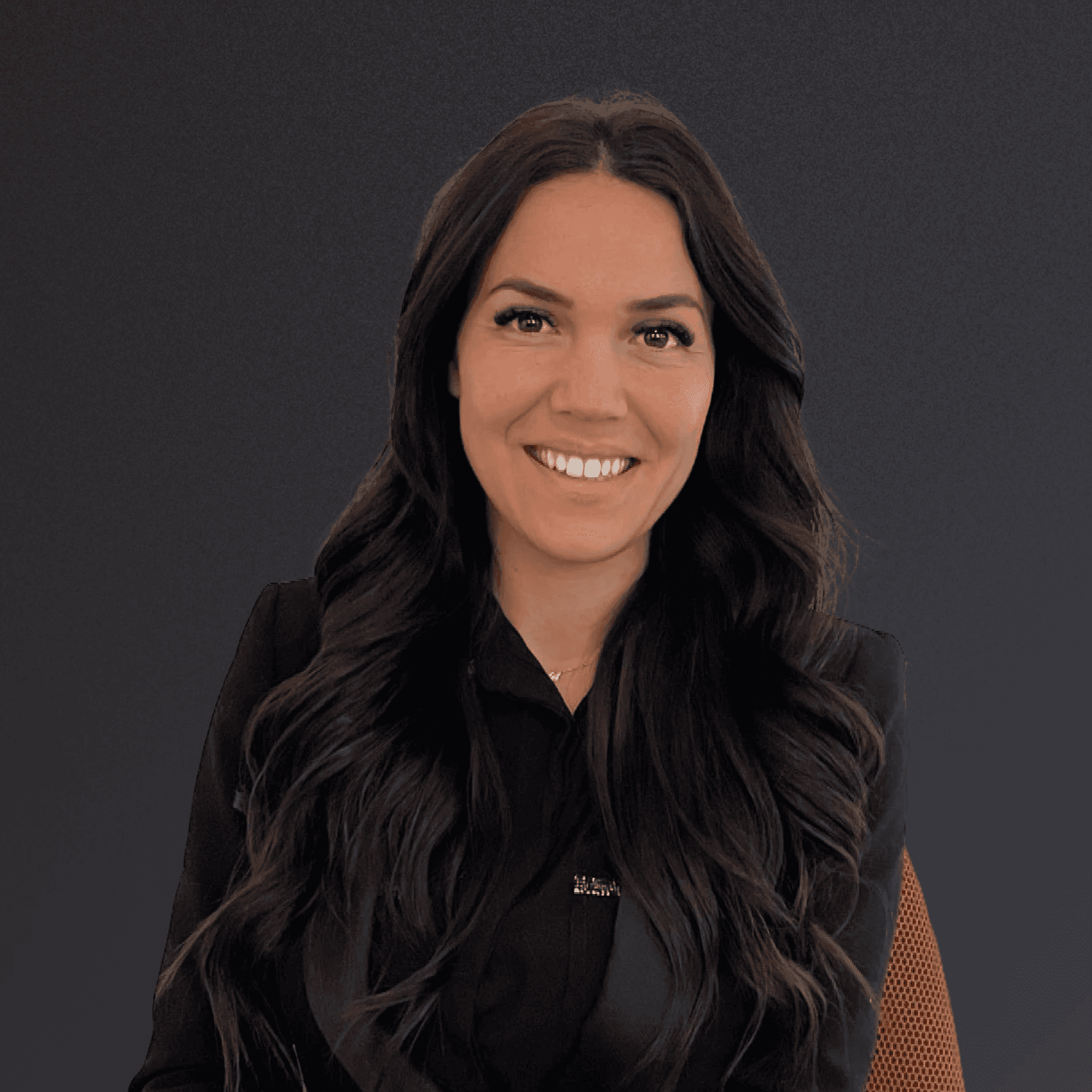 Woman with a short haircut smiling confidently, wearing a blazer and standing in warm natural light with modern architecture behind her.