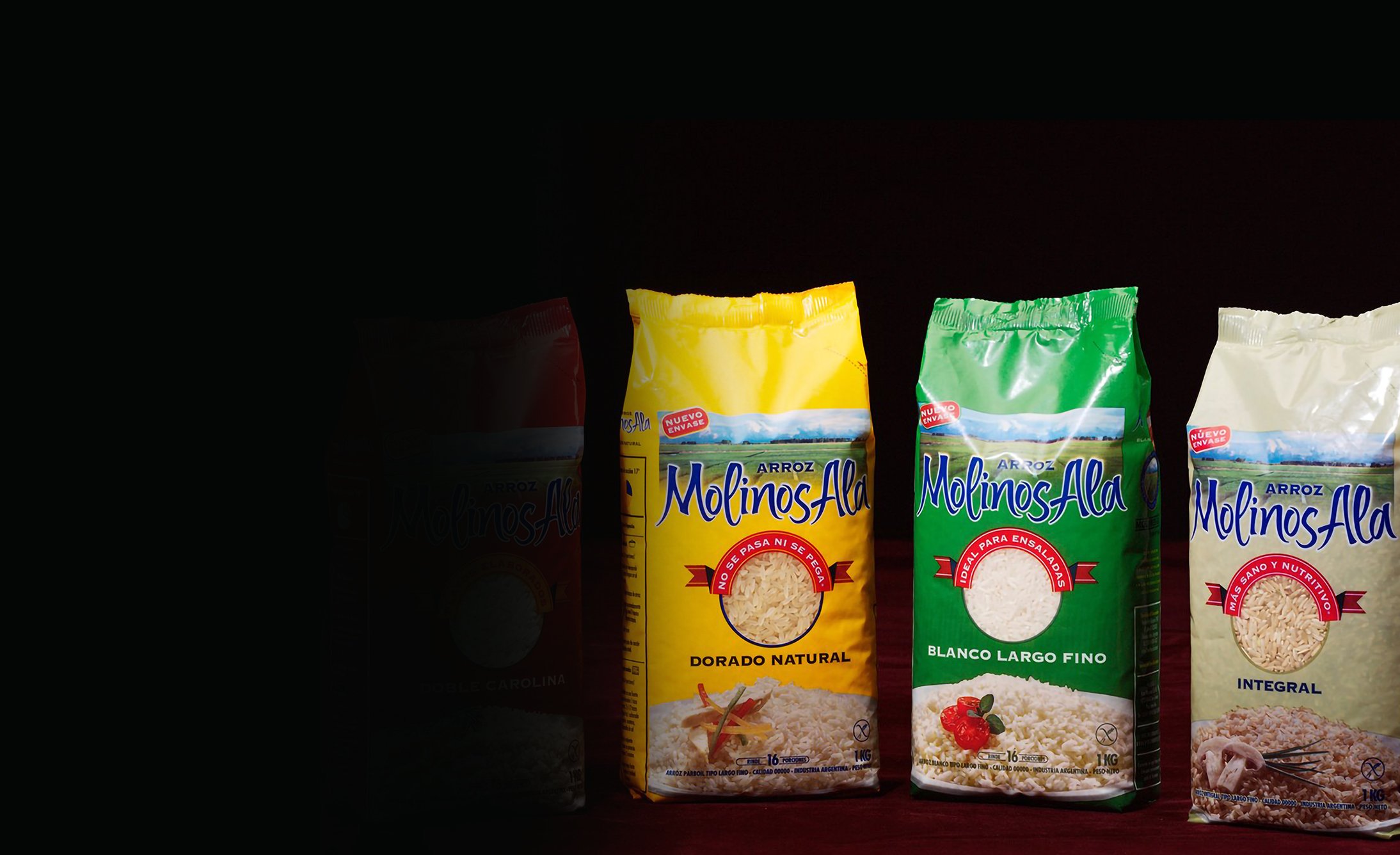 Four bags of Molinos Ala rice stand against a dark background. Each bag is a different color: red, yellow, green, and cream, featuring various rice types.