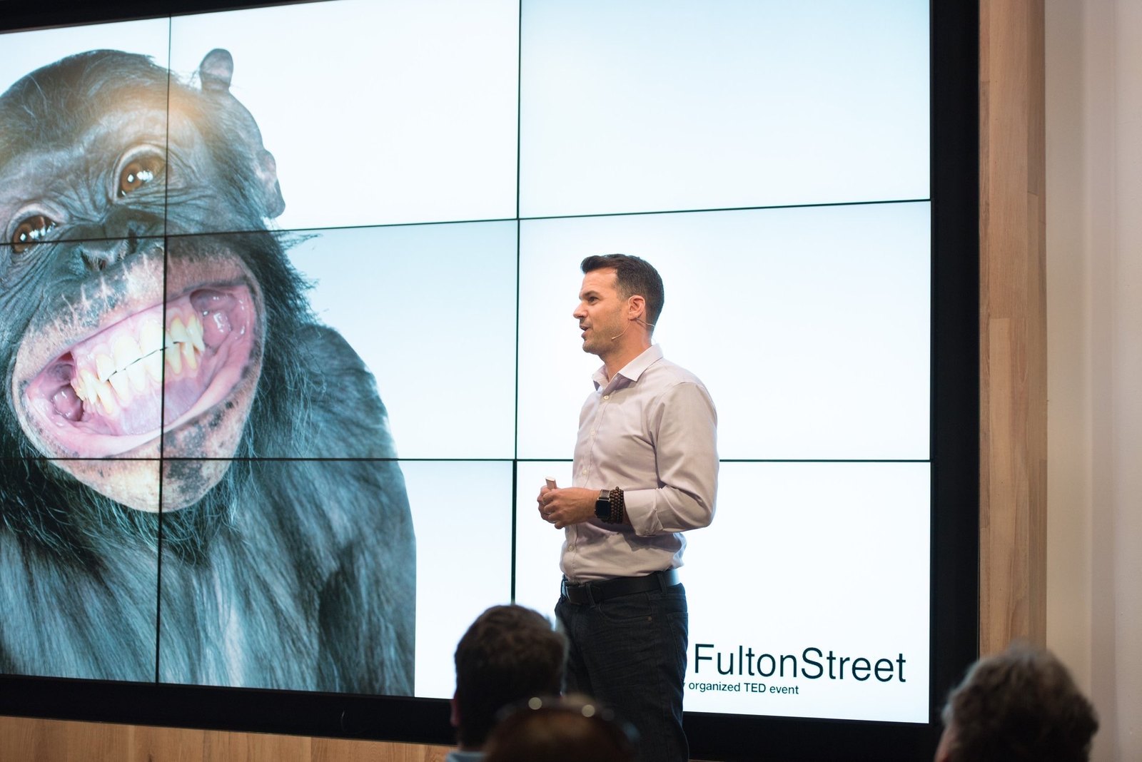 Lance Pendleton on the TEDx stage, mid-sentence beside the chimpanzee slide from his talk.