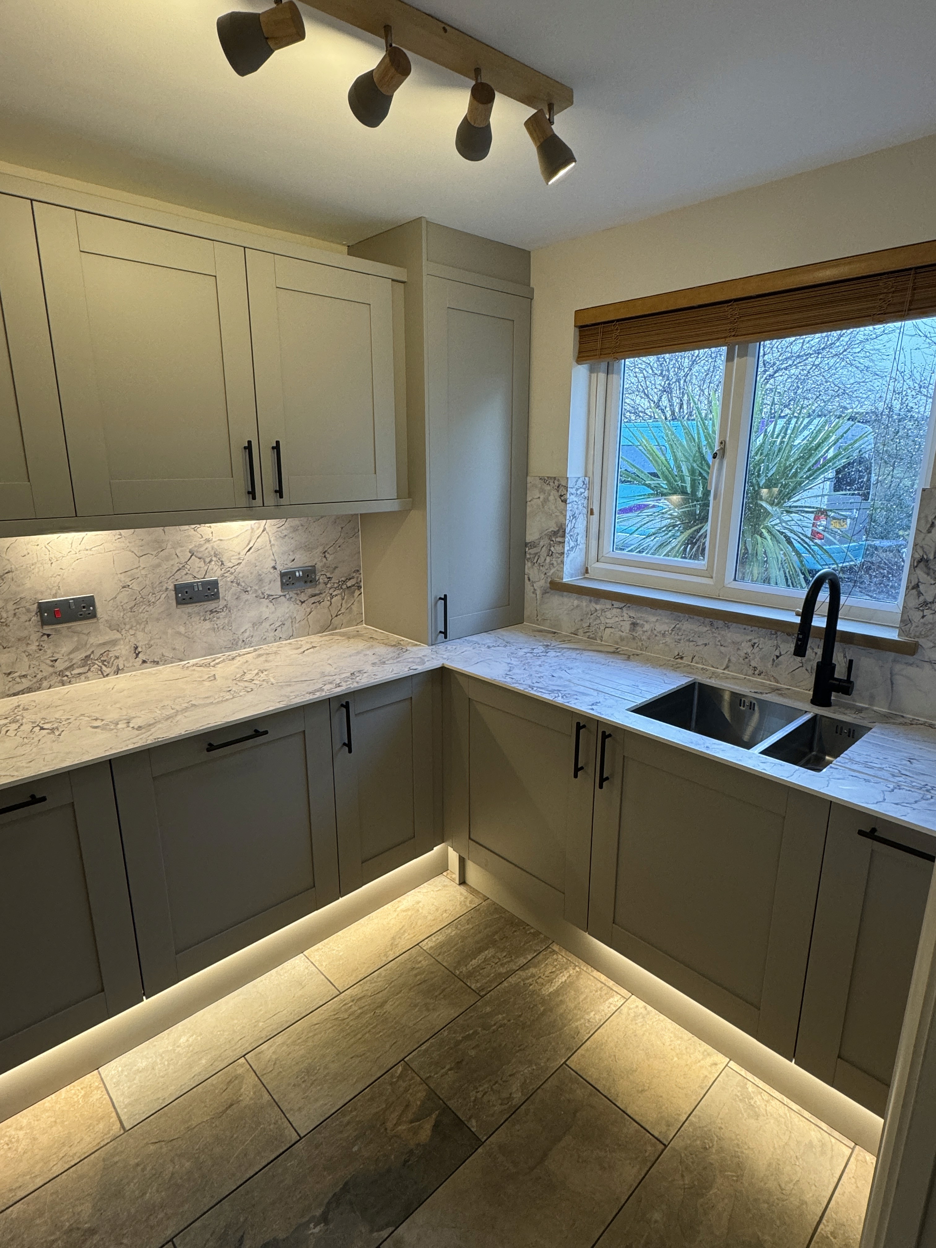 A serene outdoor seating area with two chairs, surrounded by lush greenery and a glassed-in structure.