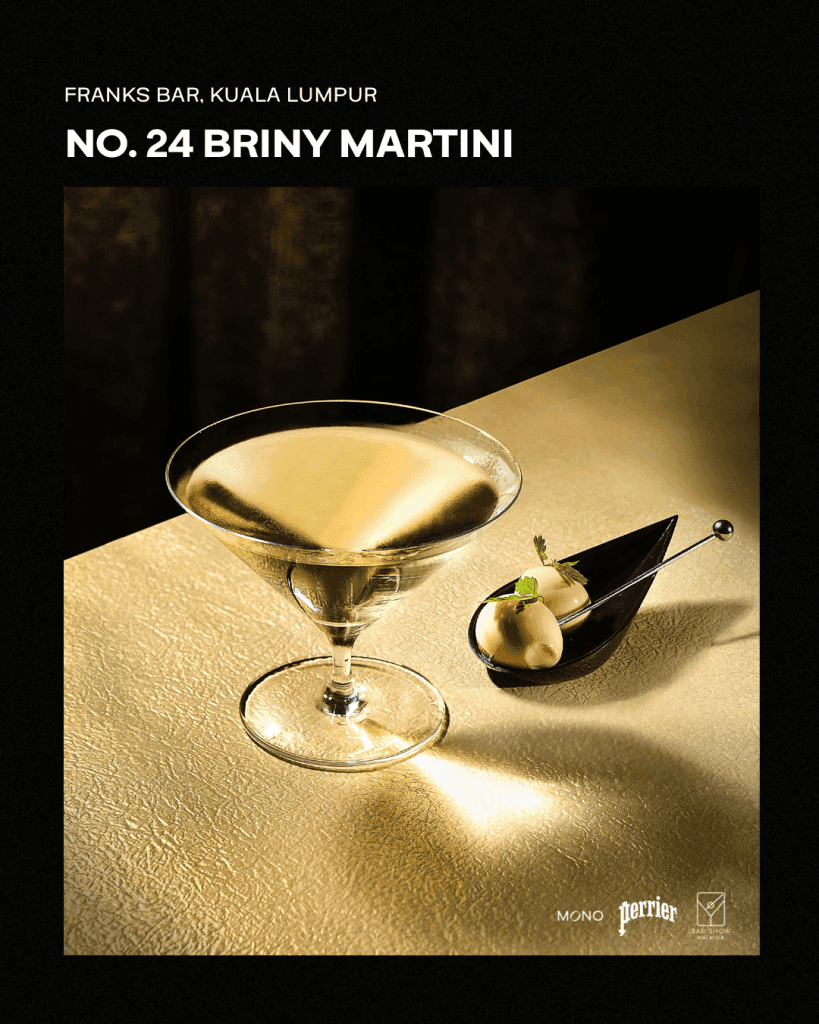 A close-up of a Briny Martini served in a elegant glass, accompanied by a small dish of garnishes, set against a textured gold background.