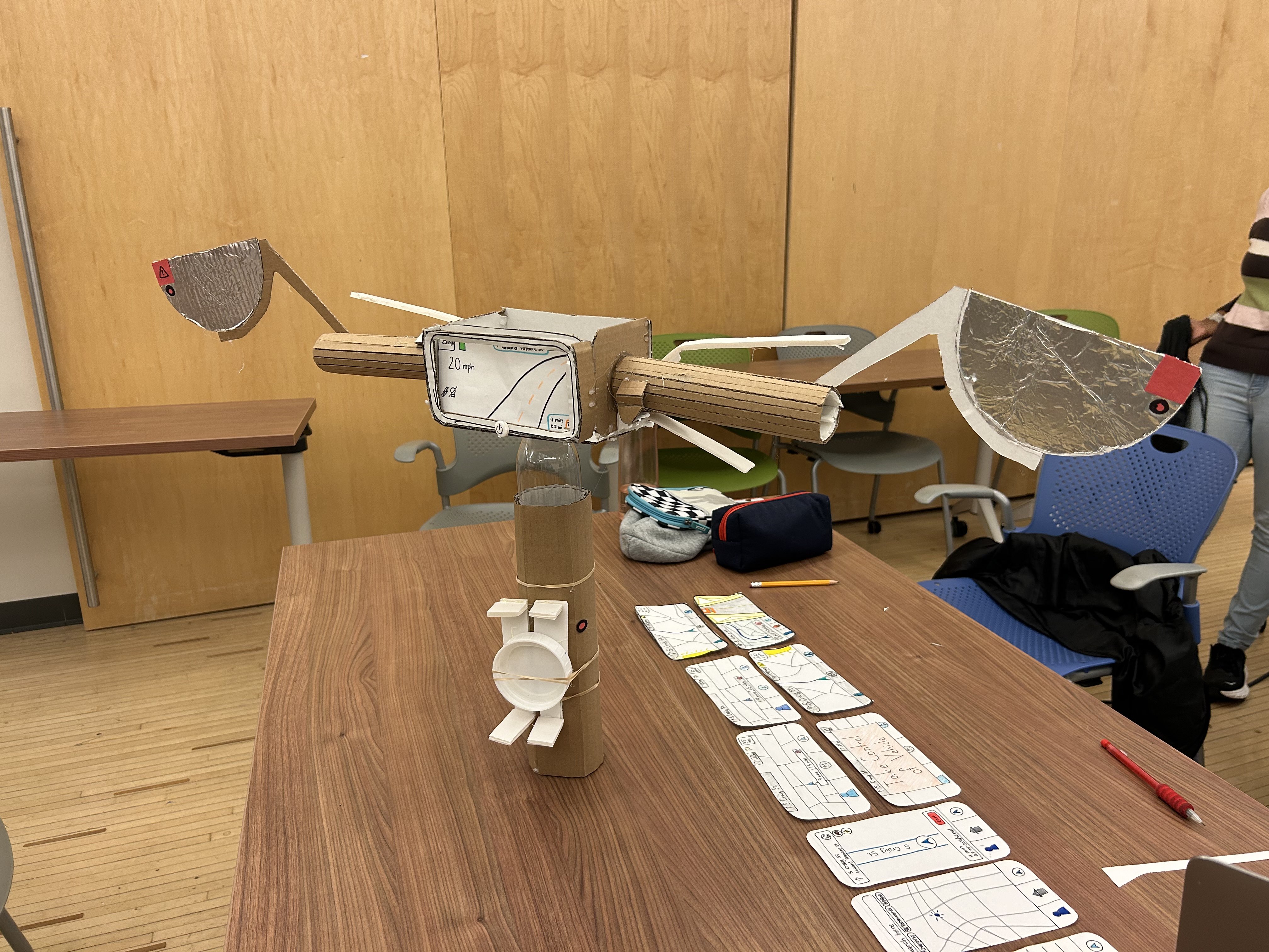 Prototype of the physical bike made primarily of cardboard and foam, with a cutout space for the dashboard, a phone holder on the steering column, mirrors with blindspot warnings on the top right, and other controls on the handles