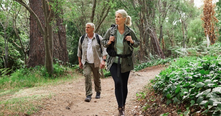 Active seniors with backpacks on a leisurely hike through a scenic forest landscape.