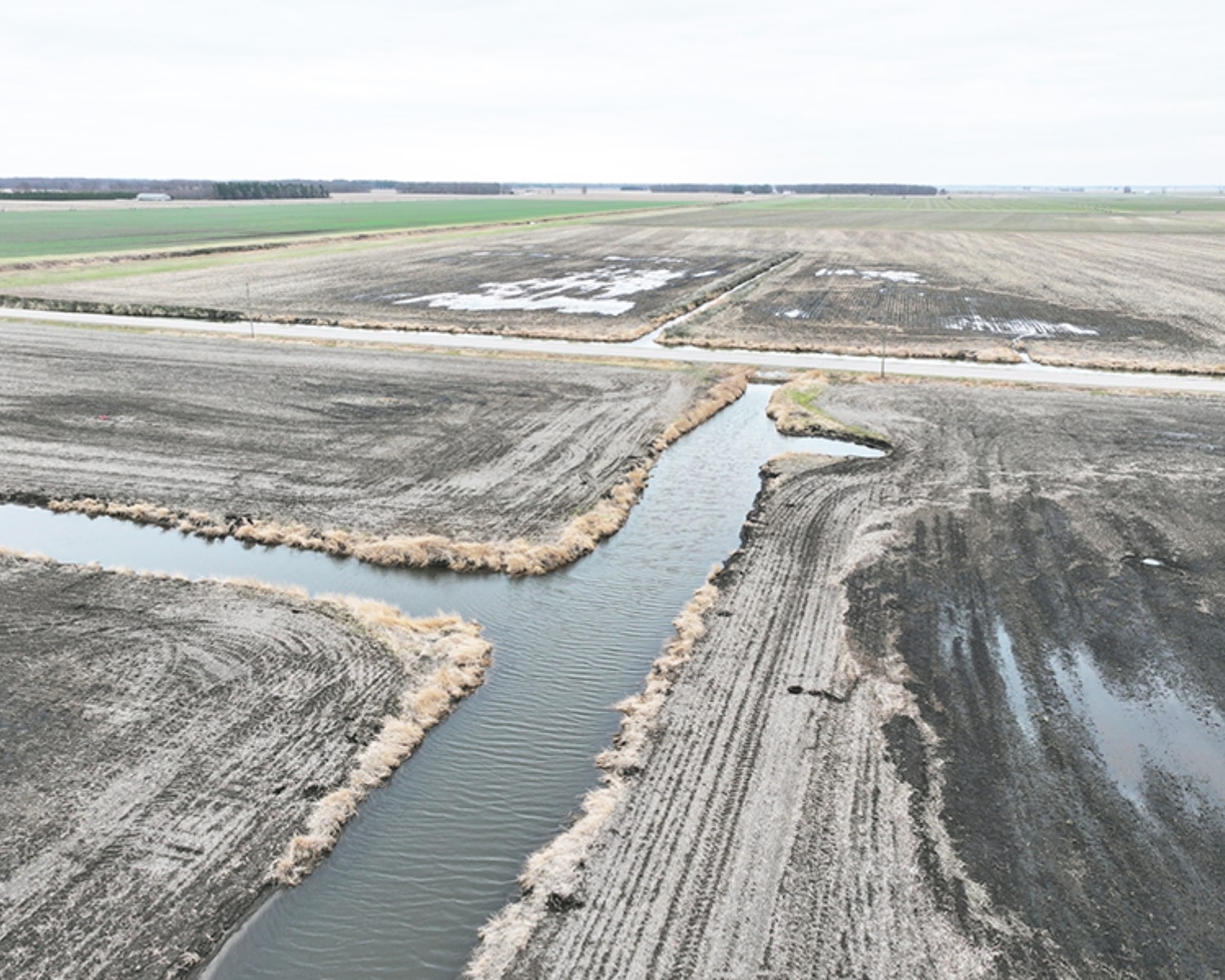 Aerial view of farmland intersected by a narrow stream and muddy fields.