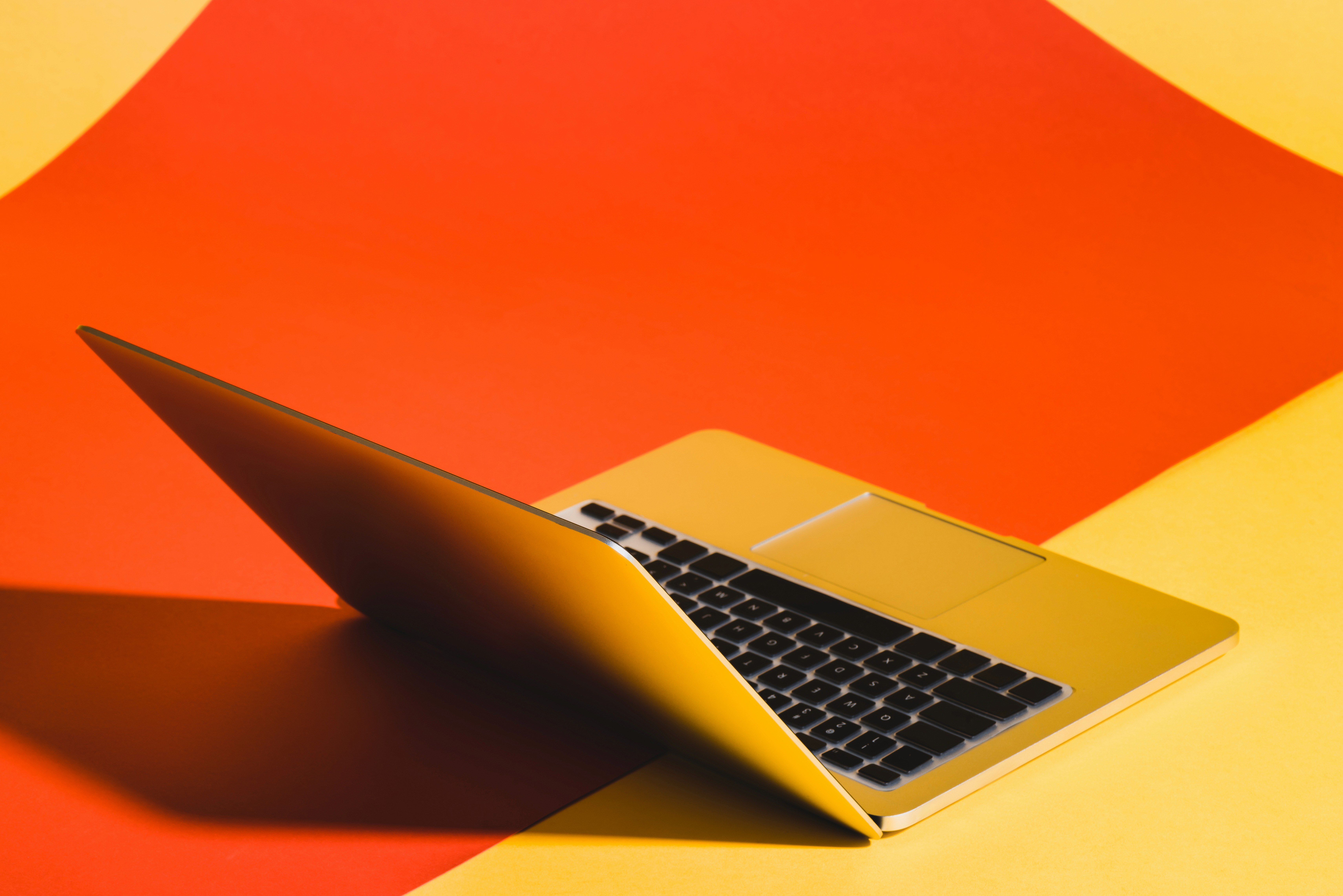 Modern gold laptop partially open on vibrant red and yellow background, showcasing creative and minimal tech workspace.