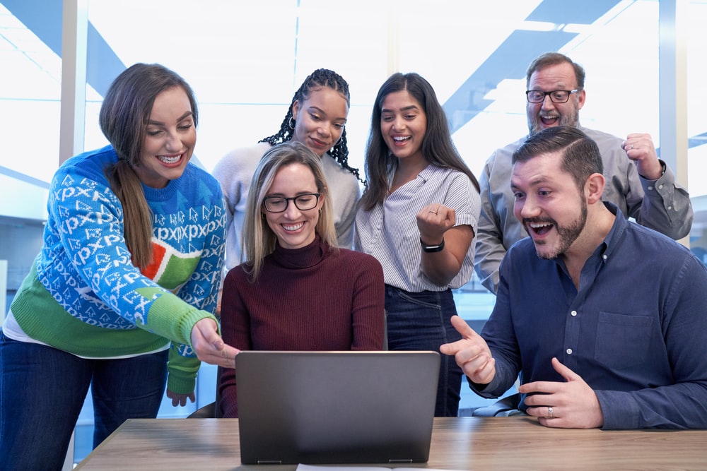 men and women sitting and standing while staring at laptop