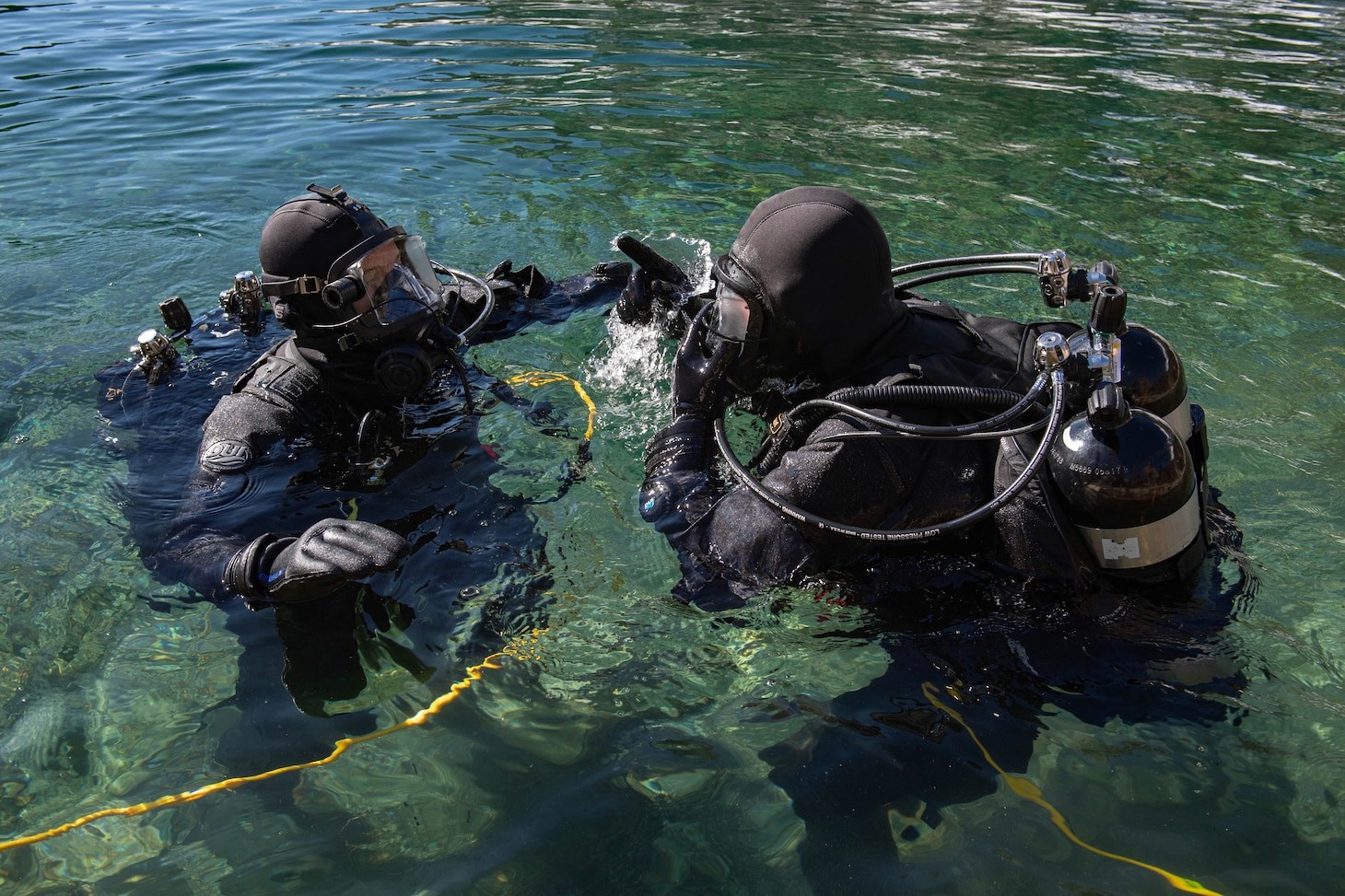 Two divers above water strapped with air tanks