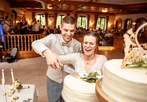 Brautpaar lacht und schneidet Hochzeitstorte gemeinsam während Feier im Saal