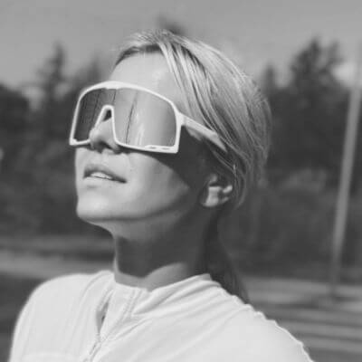 A person with light hair wearing large, modern sunglasses gazes upwards outdoors, with a blurred background of trees and sky, conveying a sense of contemplation and style.