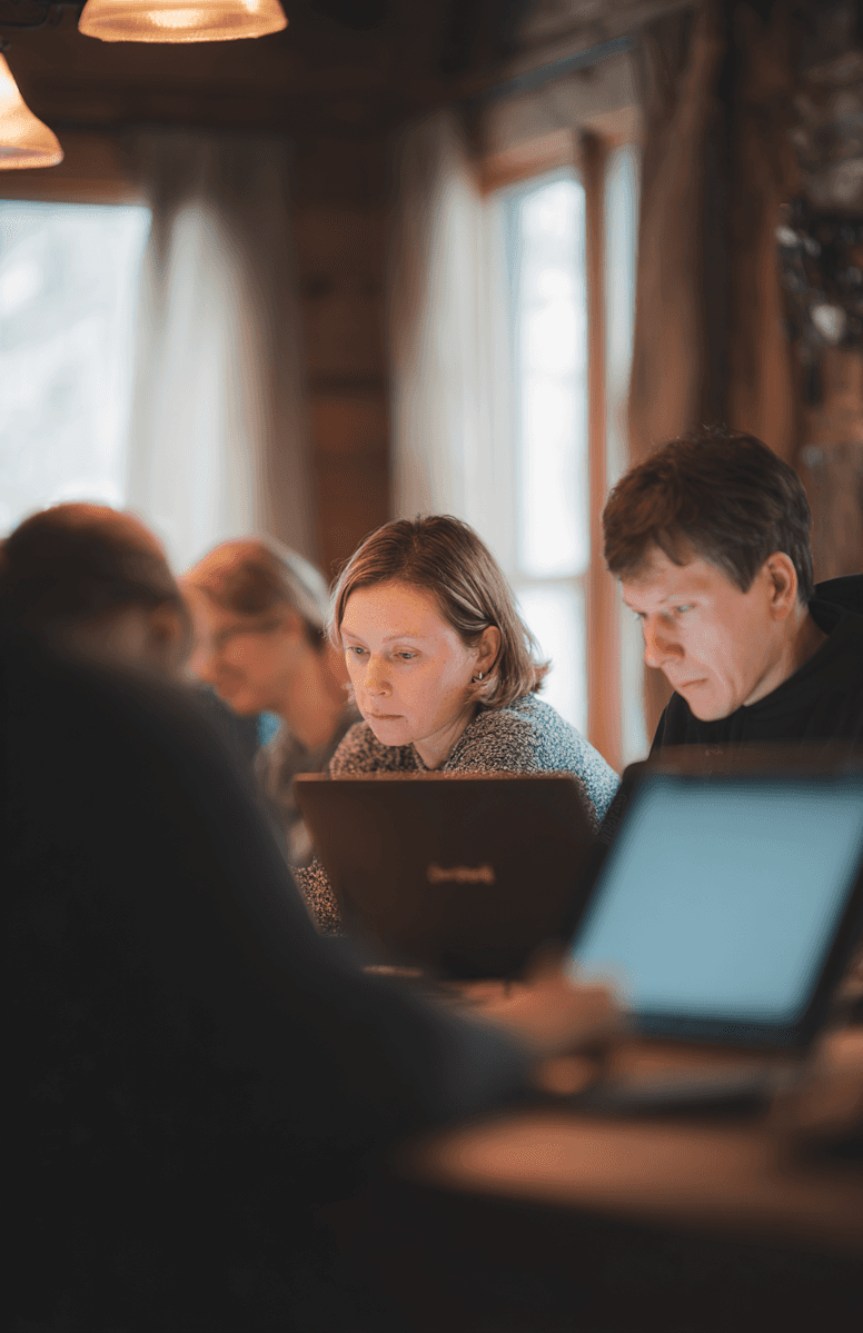A group of people working on laptops in a cozy, warmly lit room with wooden accents.