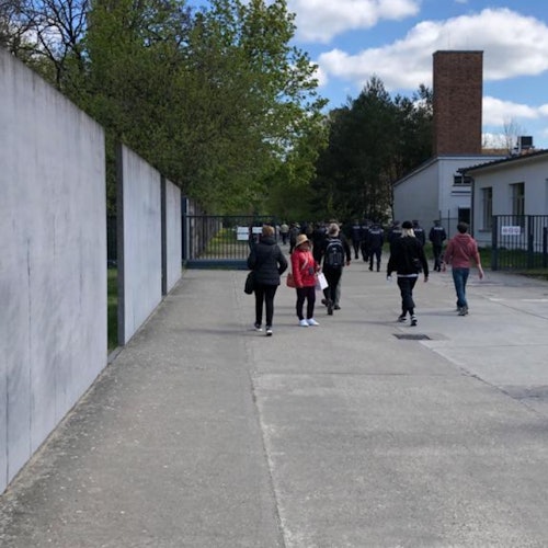 부분적으로 구름이 낀 하늘 아래, 나무와 콘크리트 벽이 있는 포장된 경로를 따라 걷는 사람들.