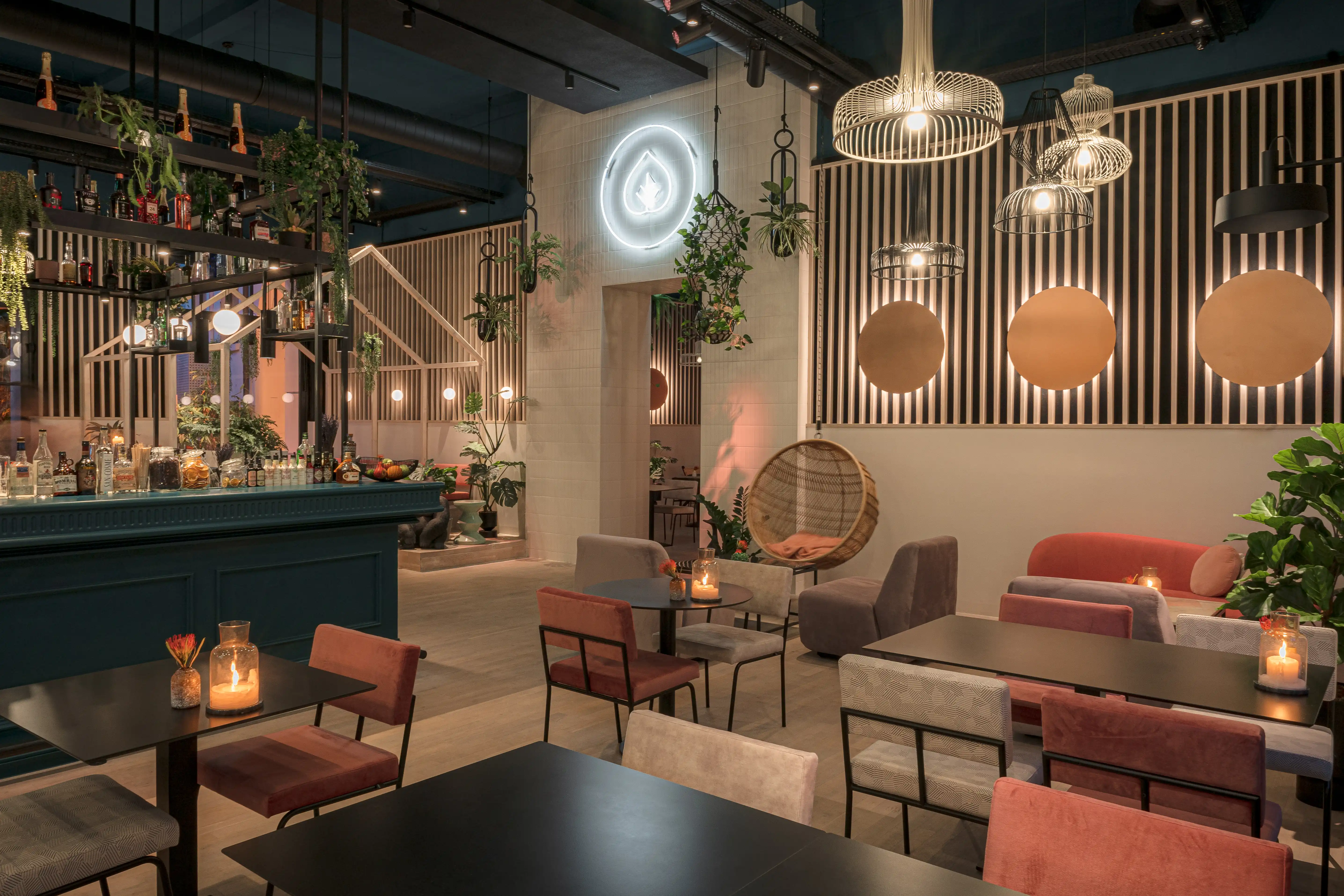 LOKAL VIER at night with the teal bar on the left, a white neon ring logo, copper circles on slatted walls, a hanging rattan chair and mixed seating with candles on tables.