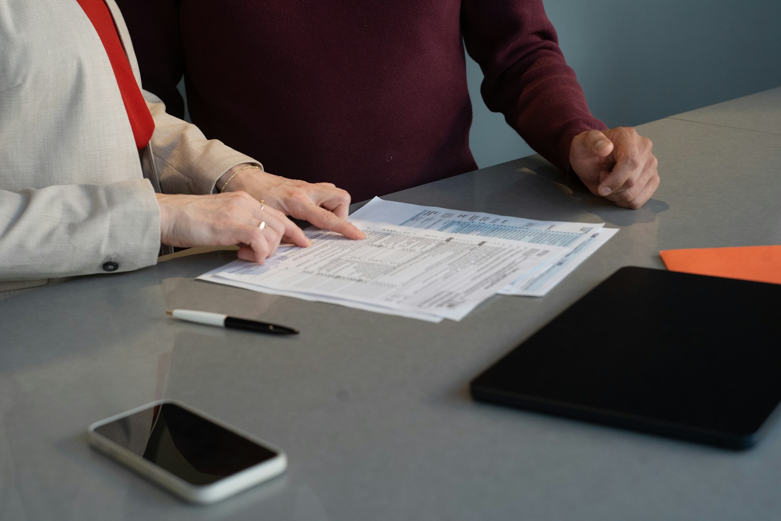 Two advisors reviewing a printed cost analysis with a client at a meeting table