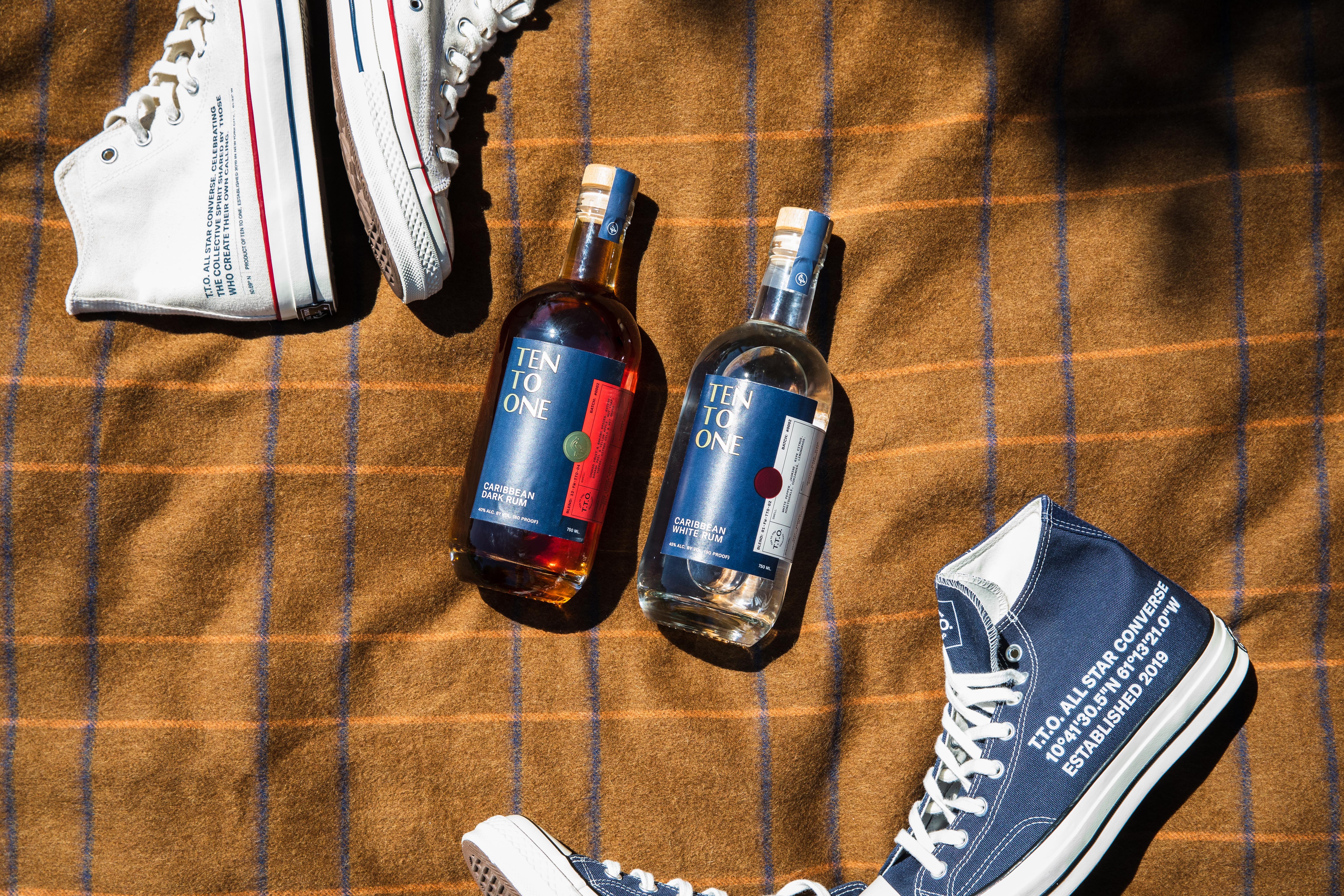 Wide flat-lay of two Ten To One rum bottles on a plaid blanket, framed by Converse sneakers for a lifestyle feel.