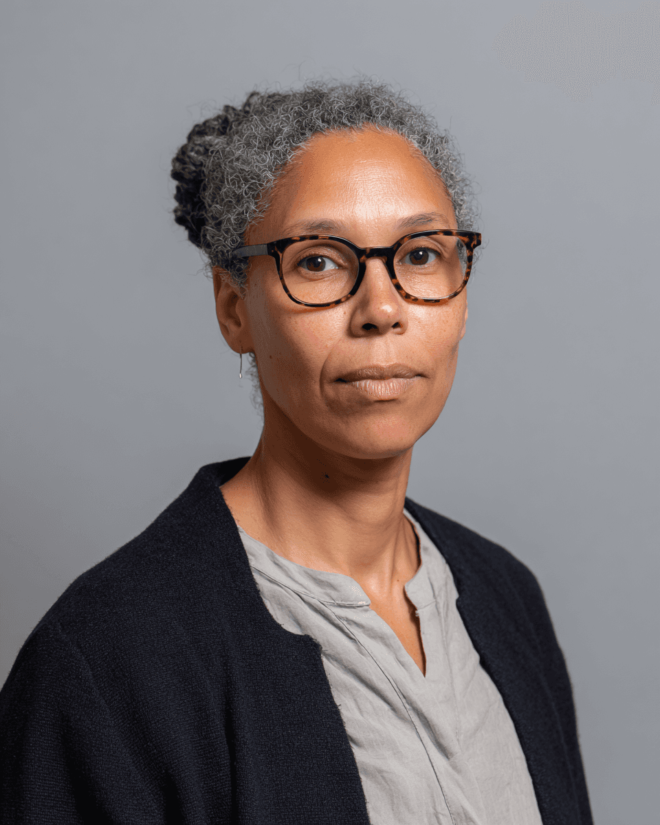 A man with dark curly hair and glasses smiling in a portrait.