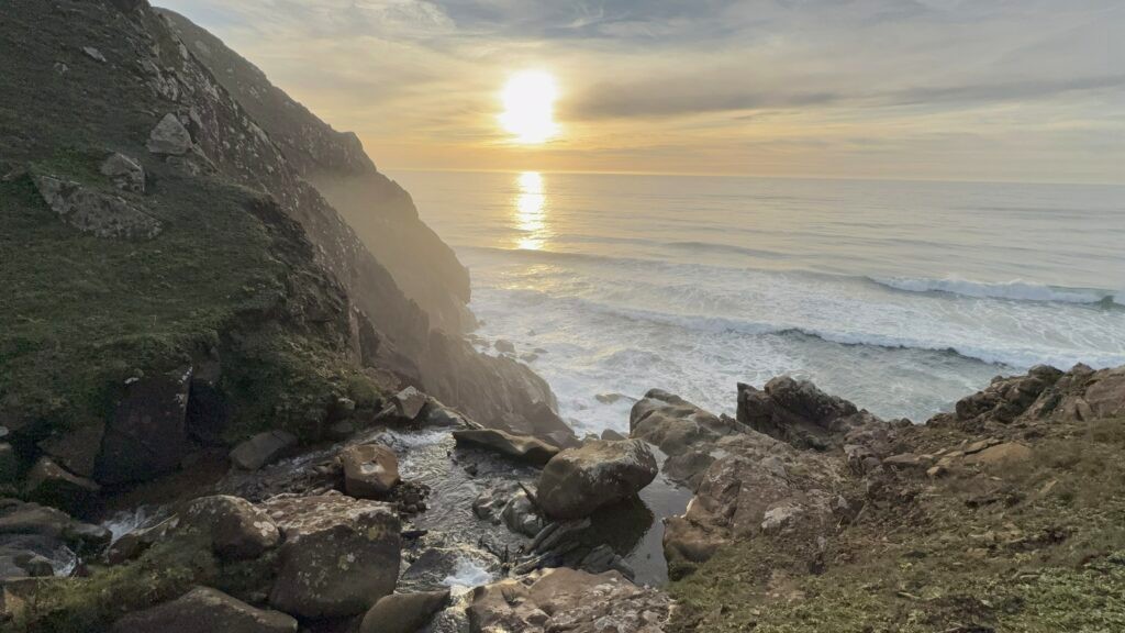 Sunset over a rocky cove and waterfall along the Gold Beach coastline