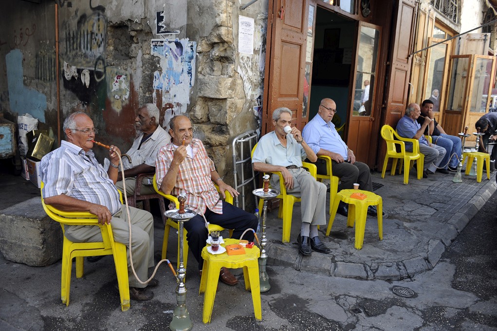 Groupe d’hommes âgés assis devant un café, fumant la chicha et discutant dans la rue, photographiés par Frédéric Bourcier.
