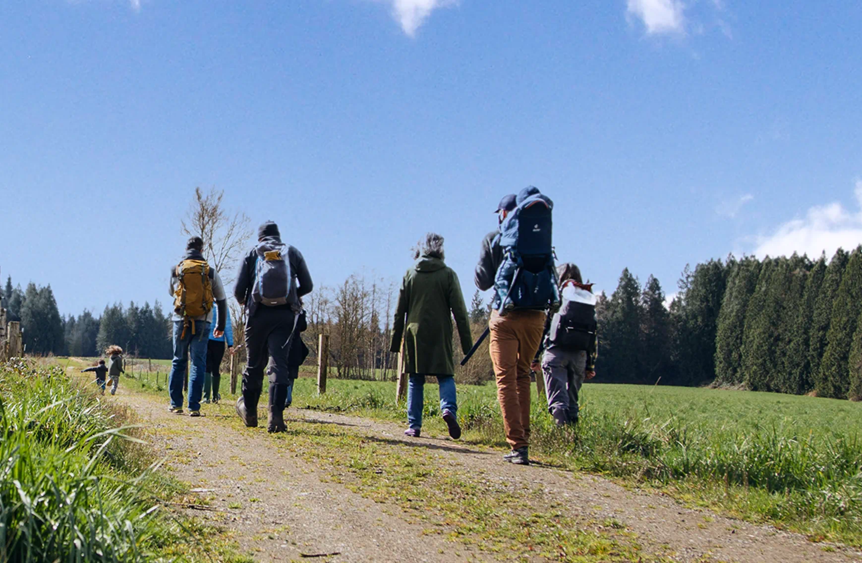A small group of people walking together along a hiking trail through the land at Rooted Northwest, surrounded by forest and open space.