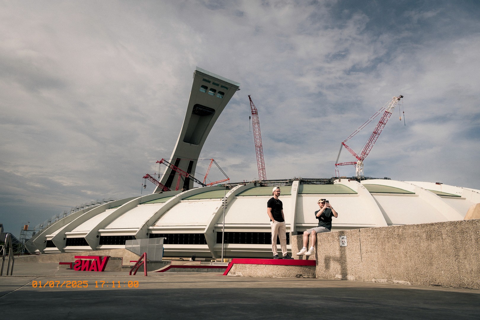 Deux hommes posent devant le Stade Olympique et ses grues.