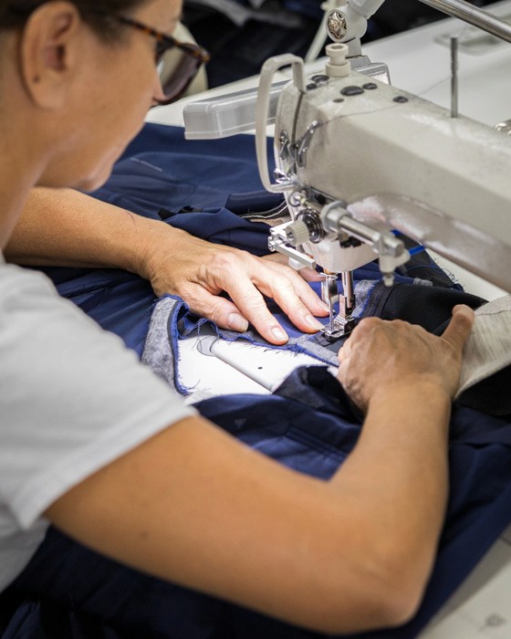 Italian tailor hand-guiding fabric through a sewing machine in the Don Marrón atelier, representing the artistry and endurance behind every piece.